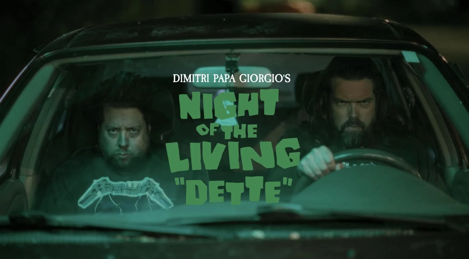 Deux hommes dans une voiture, l'un derrière le volant, avec un texte en français superposé disant 'Dimitri Papa Giorgio's Night of the Living Dente'.