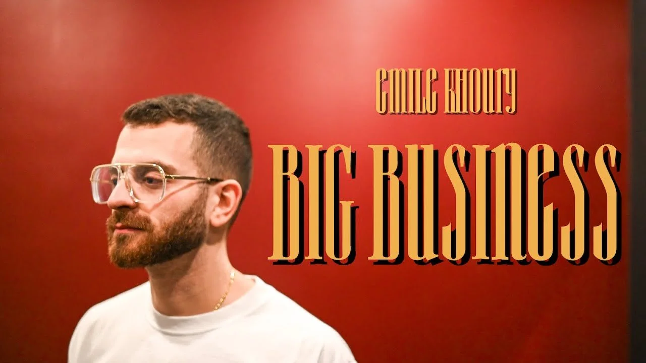 image d'un homme avec des lunettes et une barbe, portant un t-shirt blanc, devant un fond rouge, avec le texte 'GILG KHOURY BIG BUSINESS'