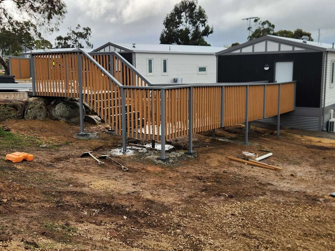 Construction of a wooden wheelchair ramp attached to a house, with tools and construction materials on the ground.