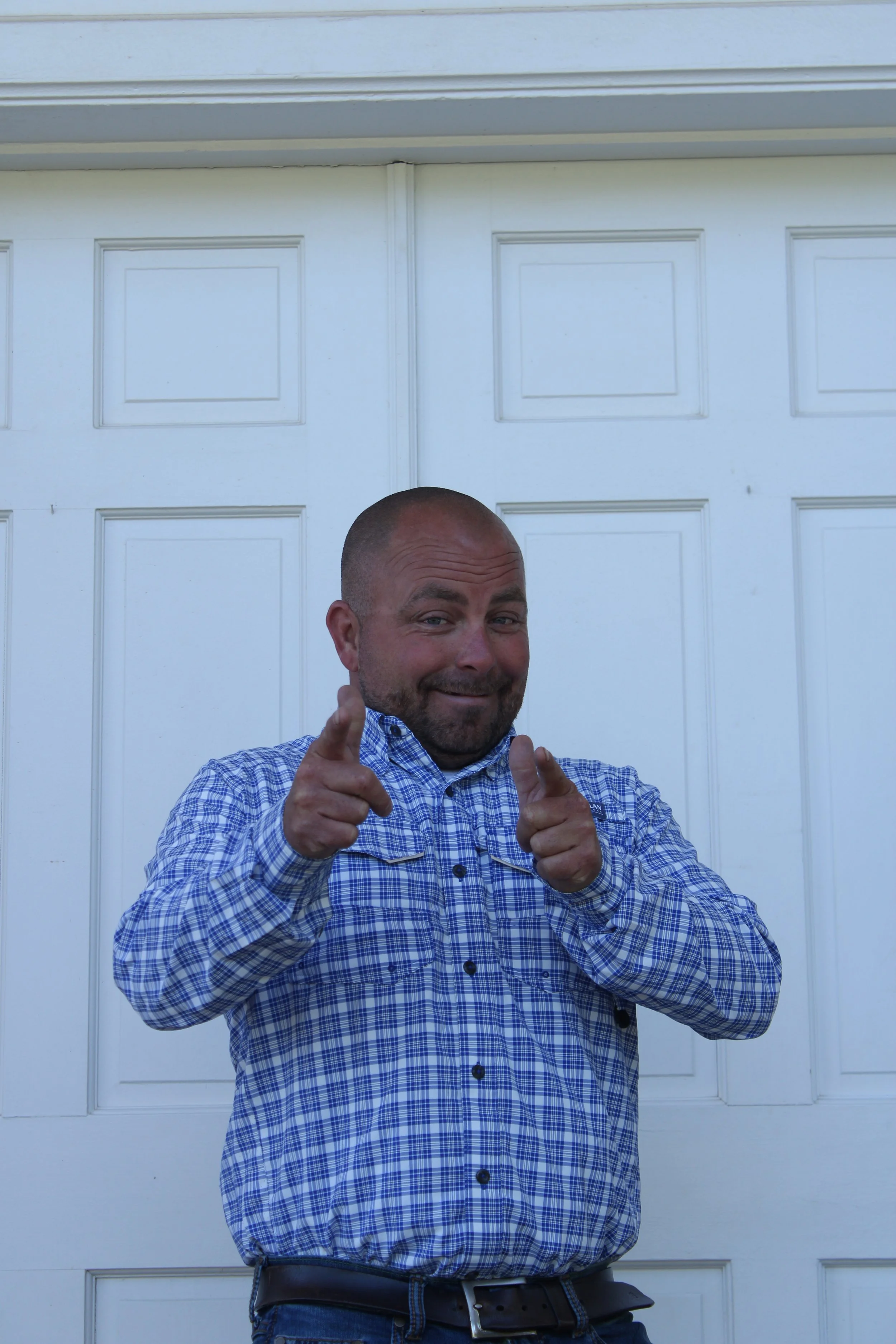 Man standing in front of a white garage door, smiling and pointing at the camera.