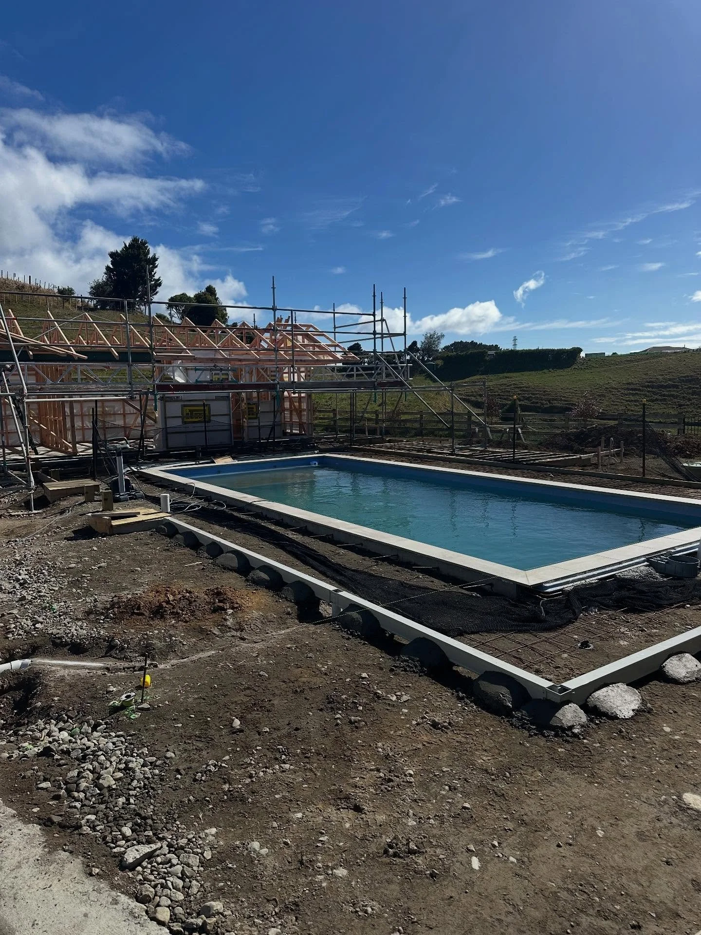 Drainage with a framed pool on muddy ground and scaffolding around a house in progress.
