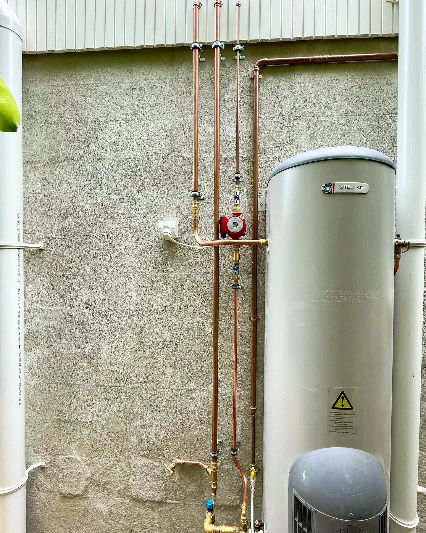 A wall-mounted water heating system with copper pipes, a large cylindrical tank, and a control pump.