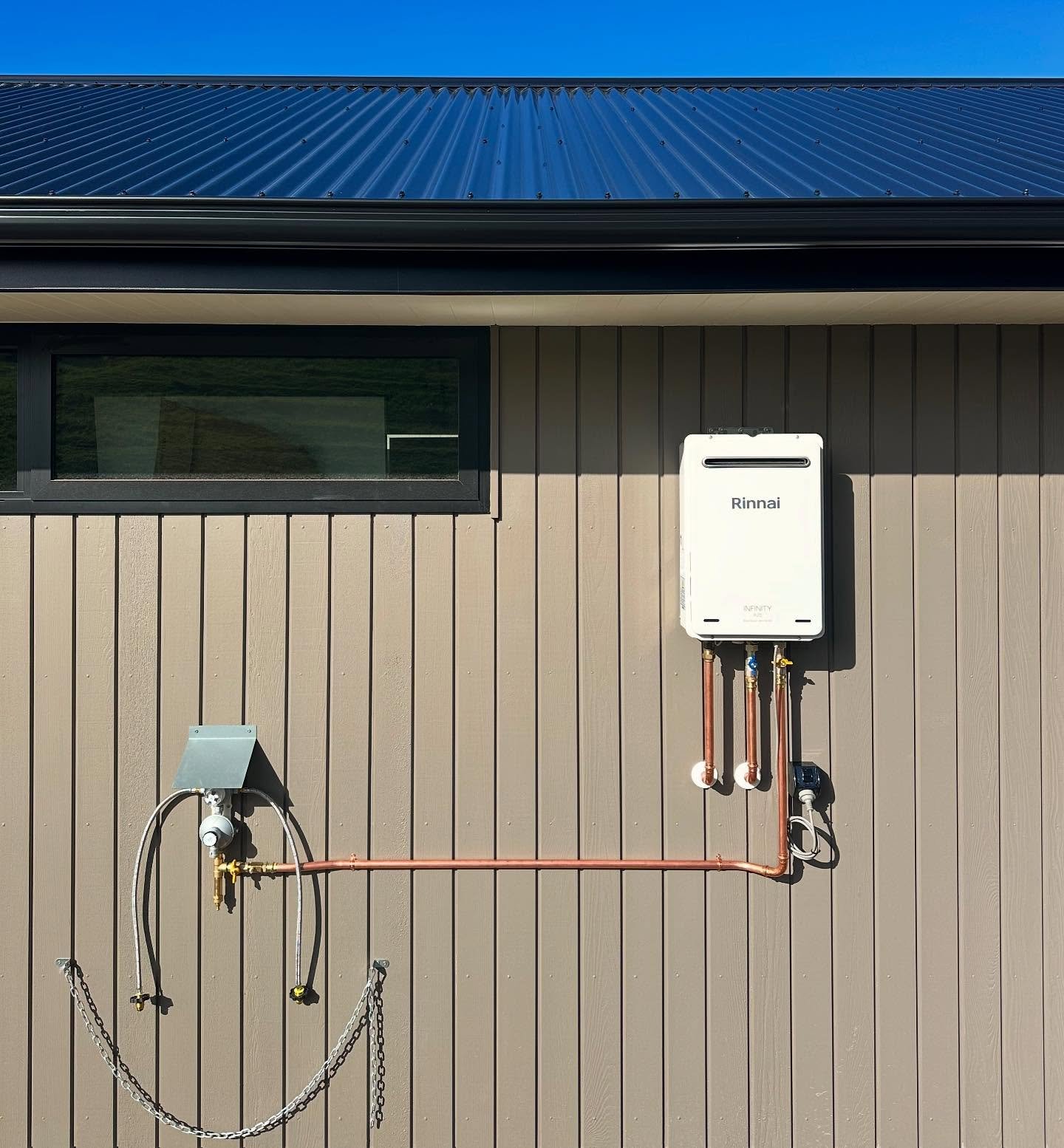 Exterior wall of a building with a window and an outdoor Rinnai water heater unit with copper pipes.