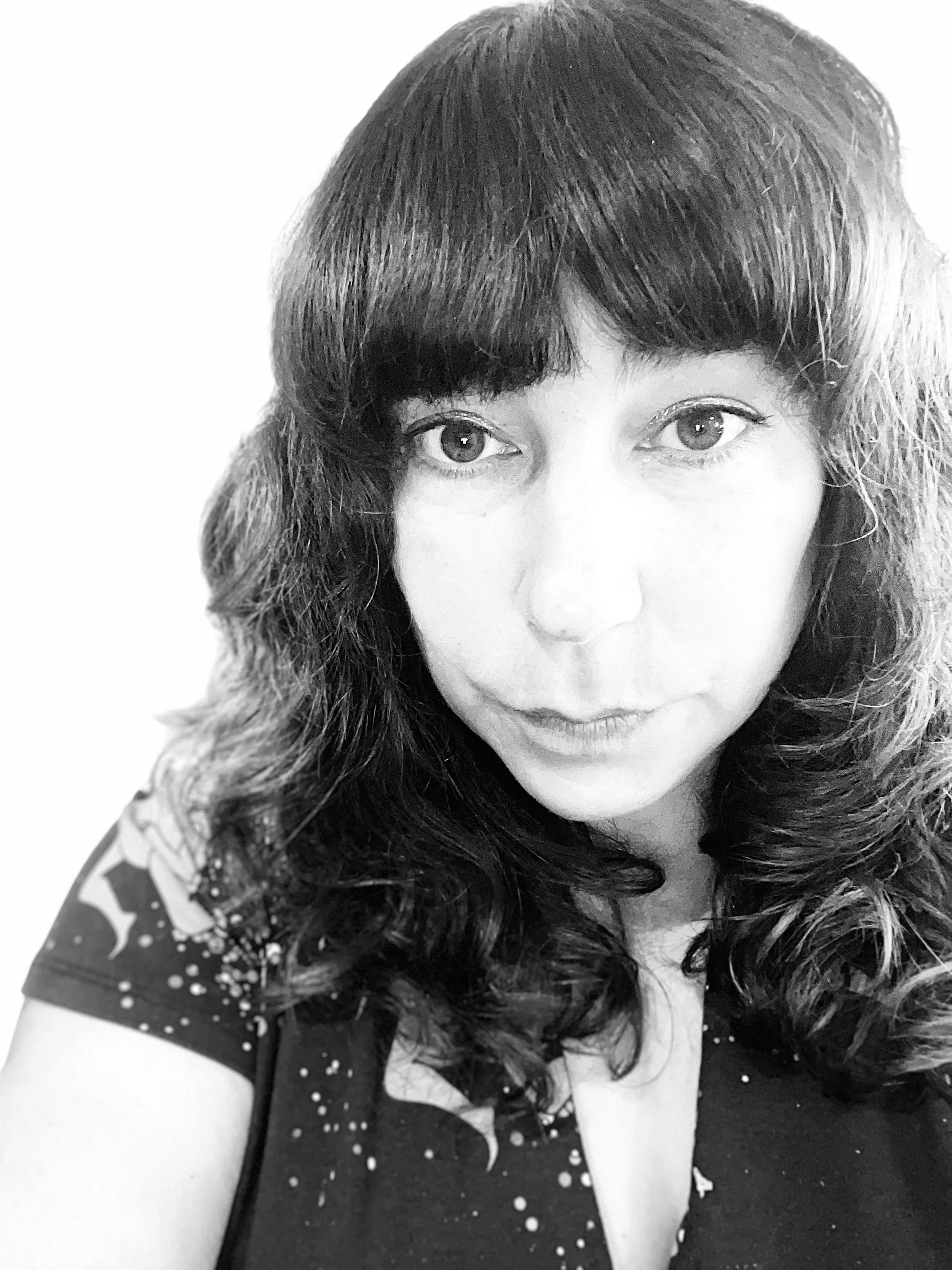 A black and white close-up photo of a woman with shoulder-length curly hair, wearing a dark top with a star pattern, looking directly at the camera.