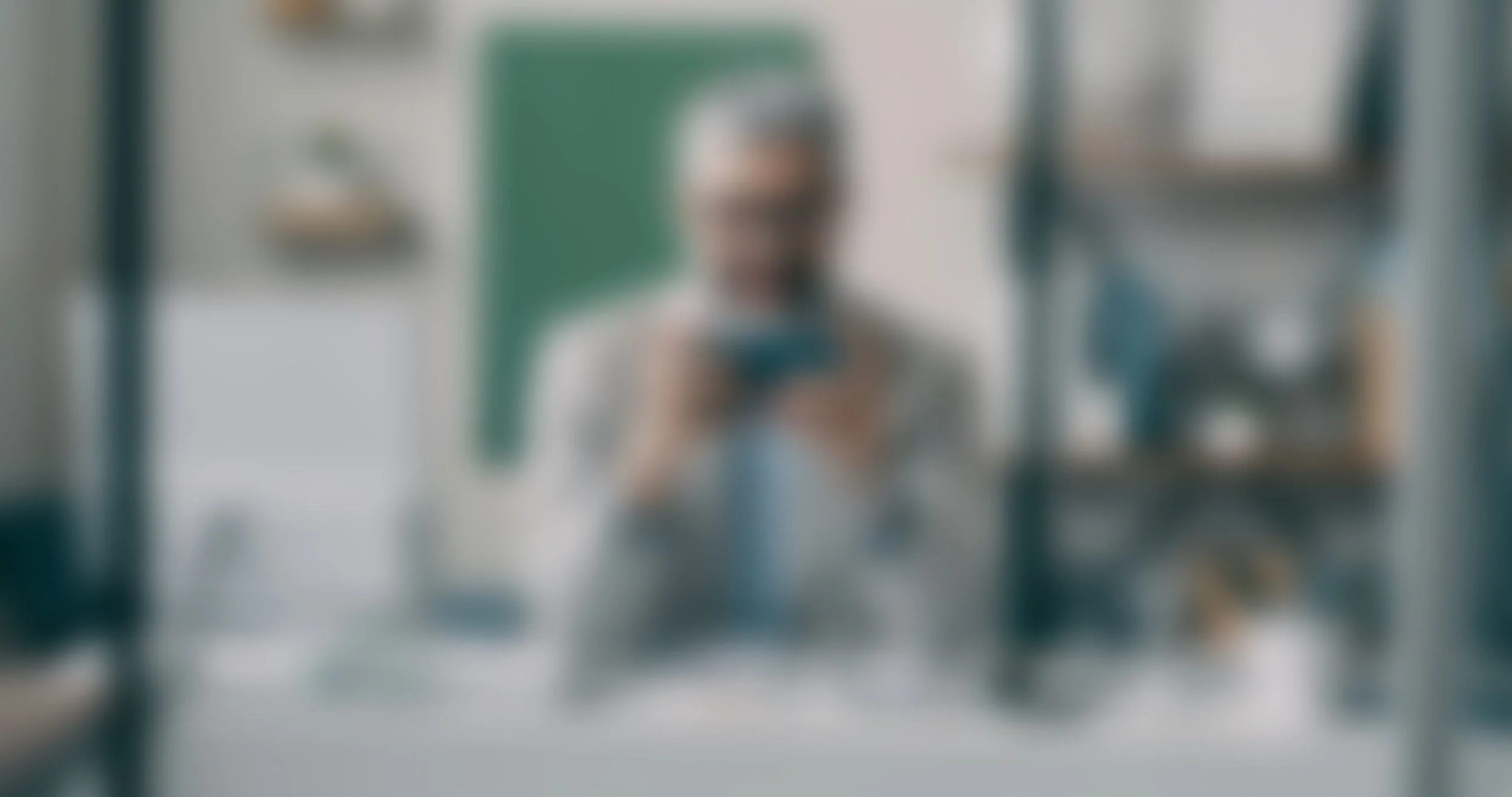 A person taking a photo of themselves in a mirror, with shelves and a green bulletin board in the background.