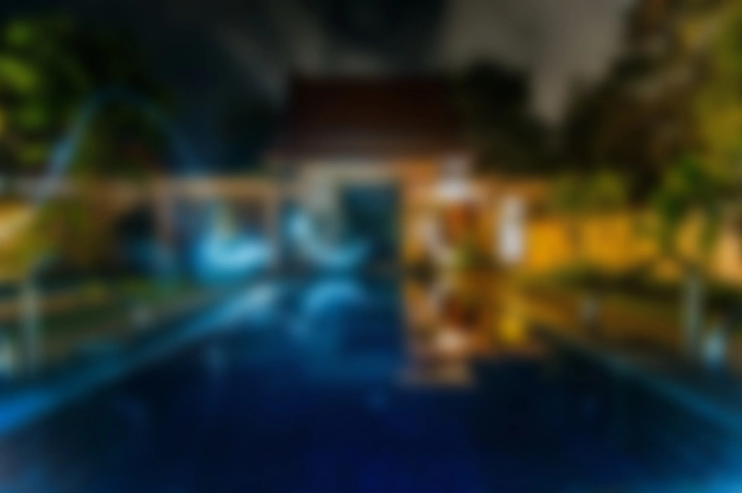 Blurred image of a swimming pool with a house and trees in the background.