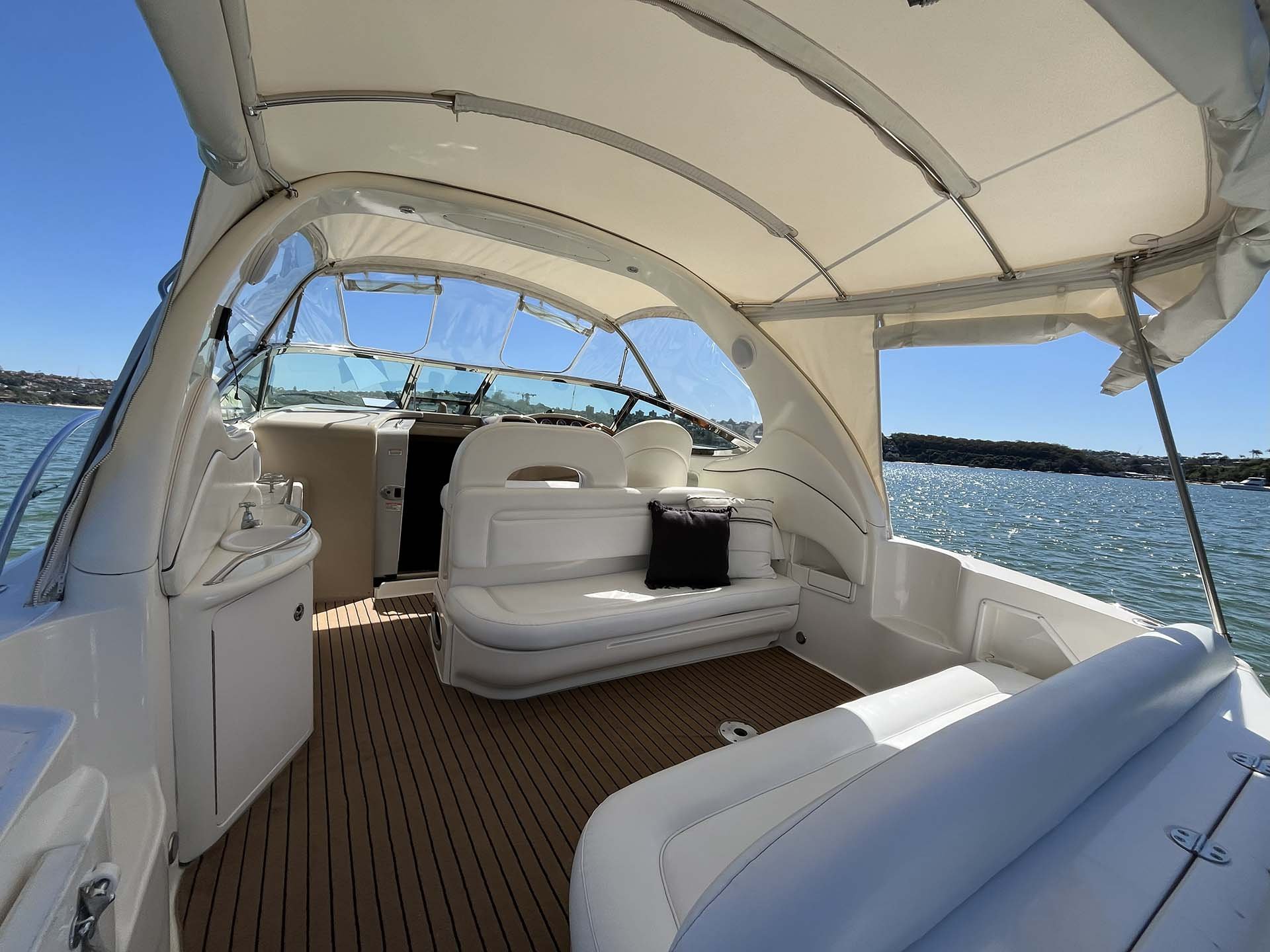 Inside view of a Opal with white cushioned seating, and a shaded canopy, on clear waters with a shoreline in the distance.