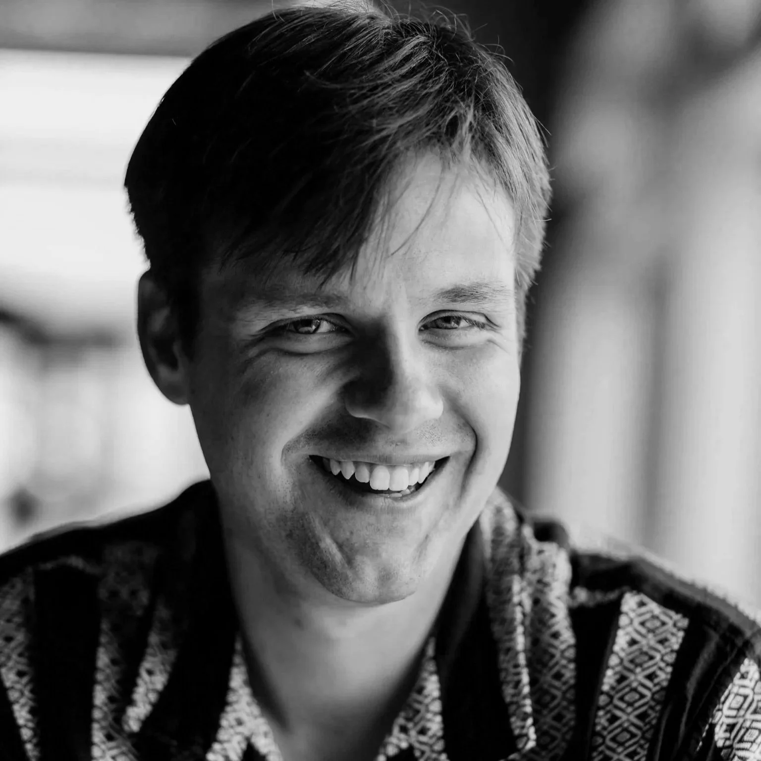 A photo of playwright, Hans Bloedel: a man with short hair, wearing a patterned shirt, in black and white.