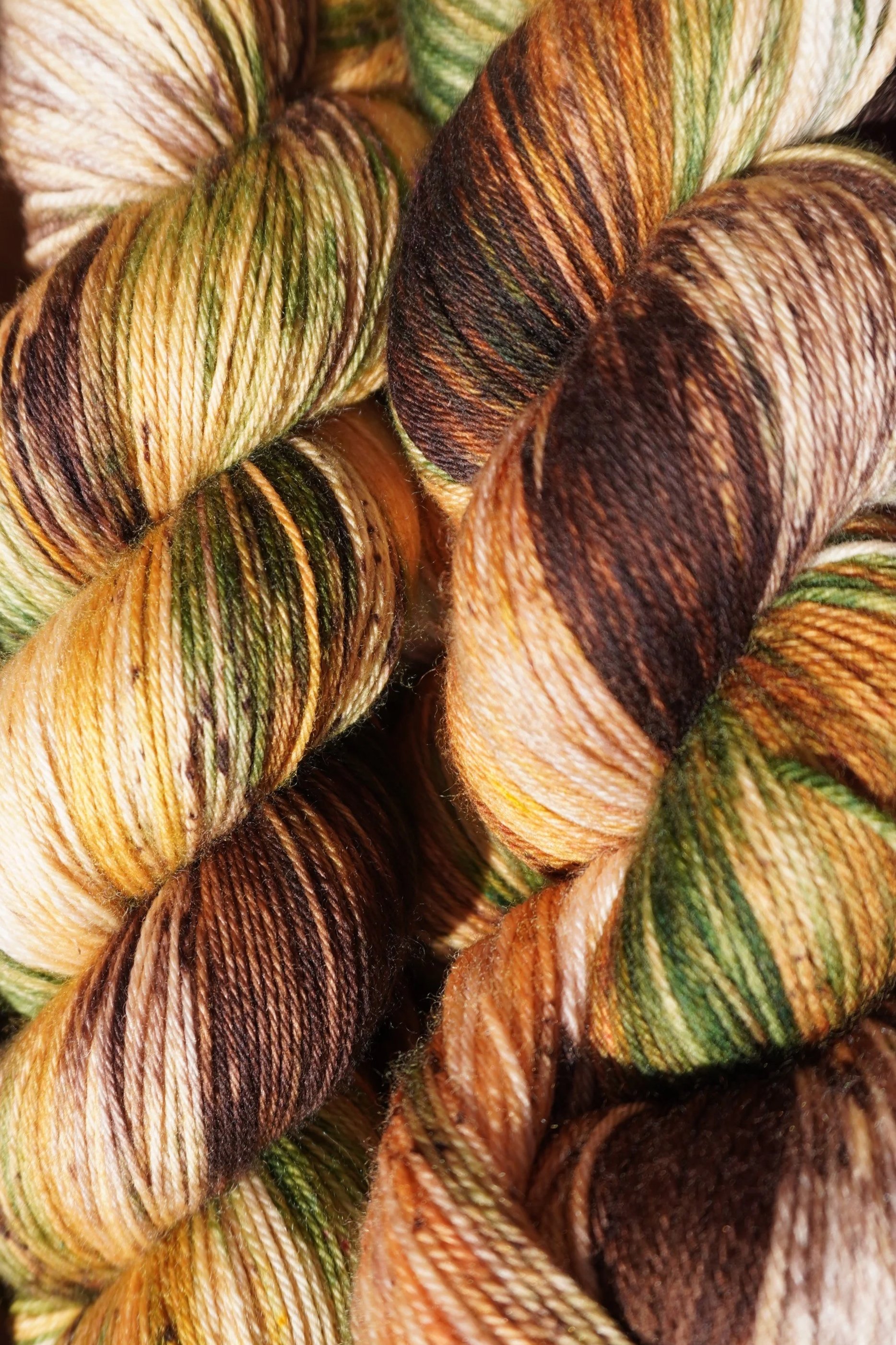 Close-up of twisted skeins of multicolored yarn in shades of brown, tan, green, and cream.