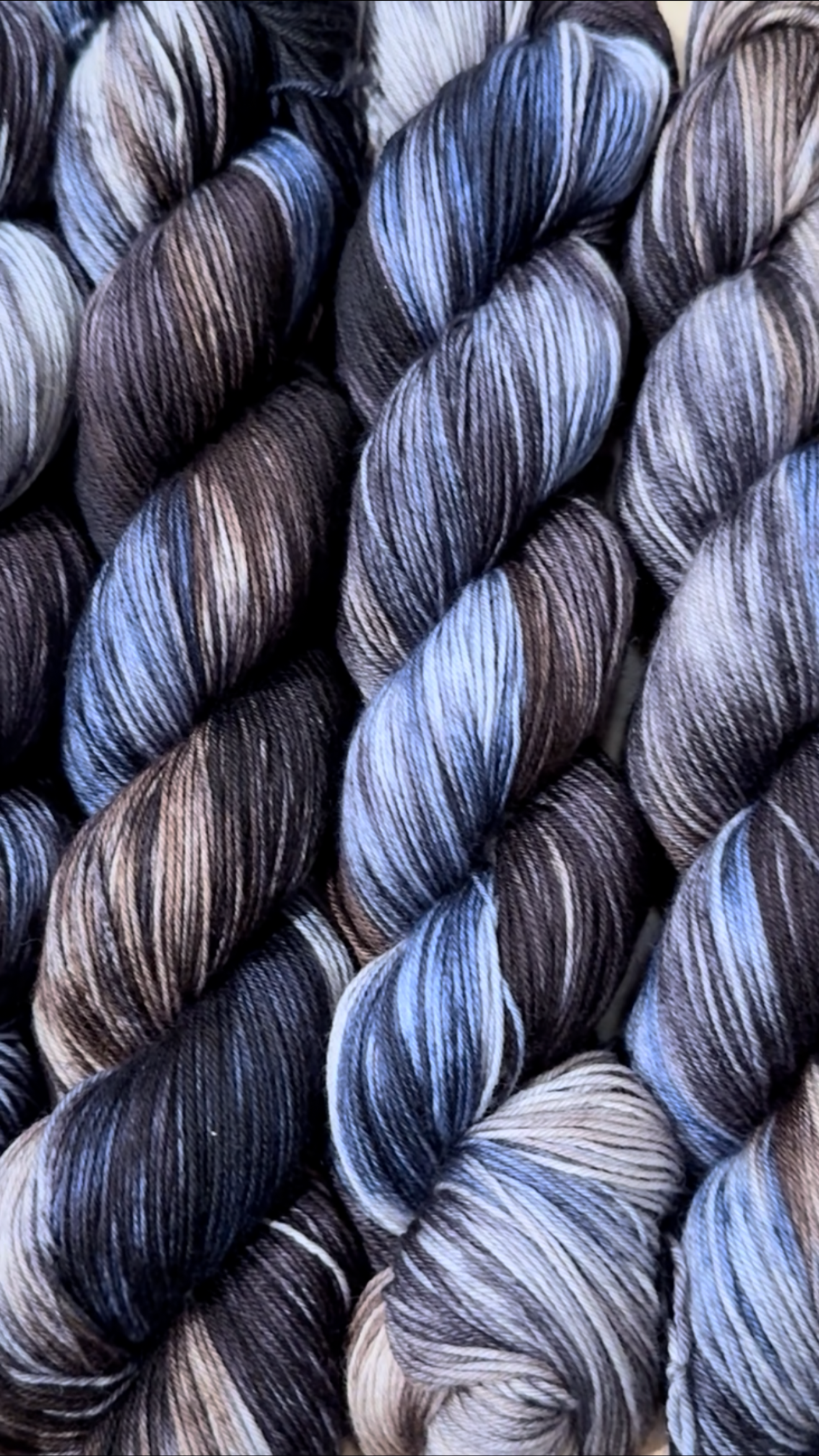 Close-up photo of tightly wound skeins of multicolored yarn in shades of brown, black, gray, and beige.