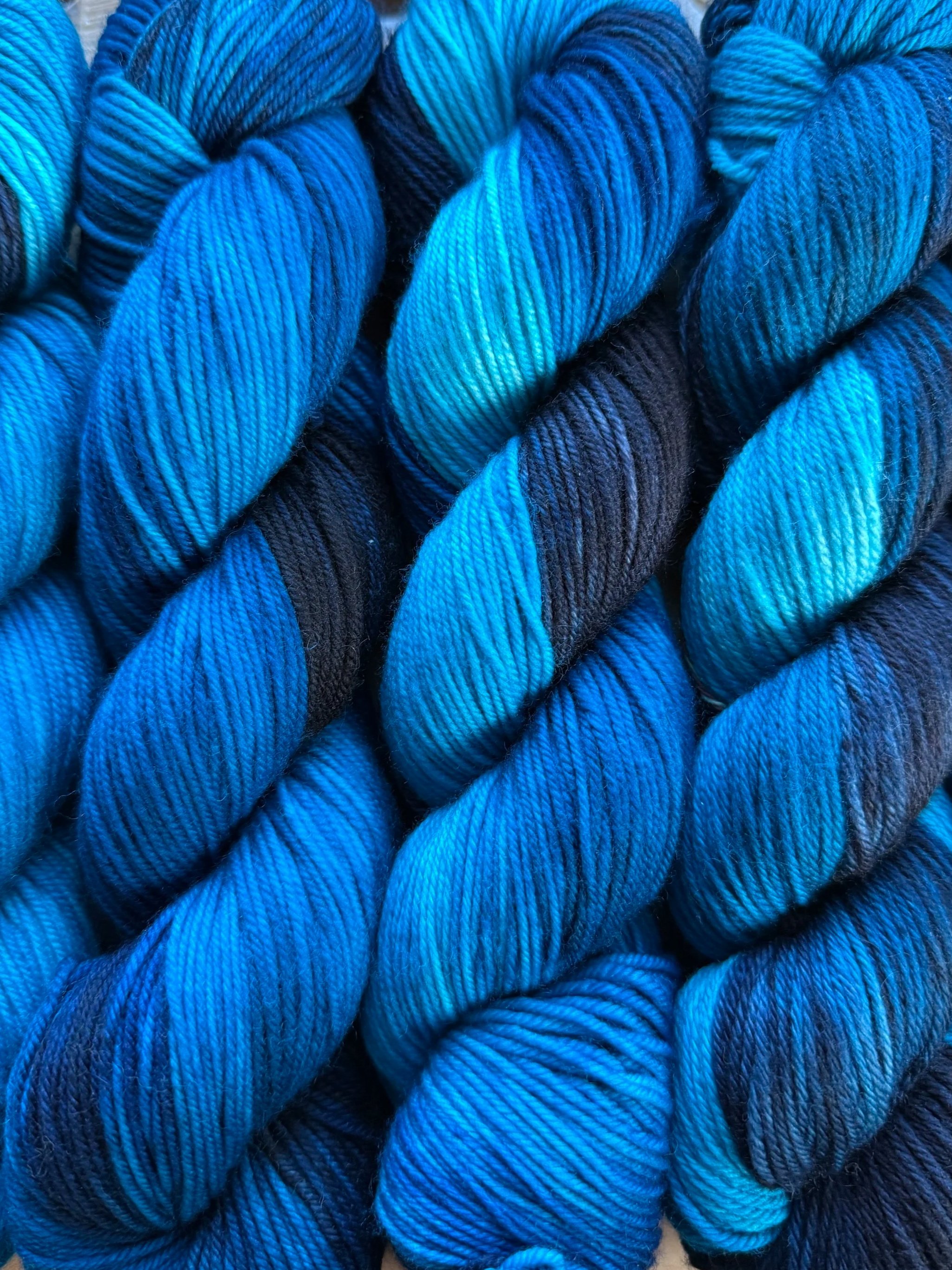 Multiple skeins of blue and black yarn twisted together, arranged side by side.