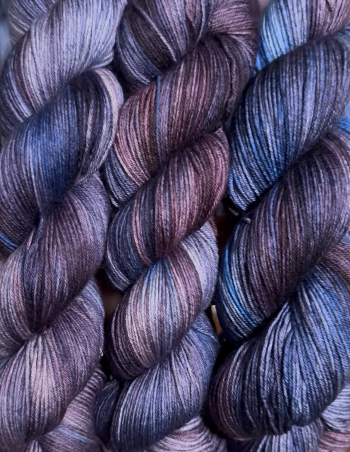 Close-up of several twisted skeins of multicolored yarn with shades of purple, blue, and pink.