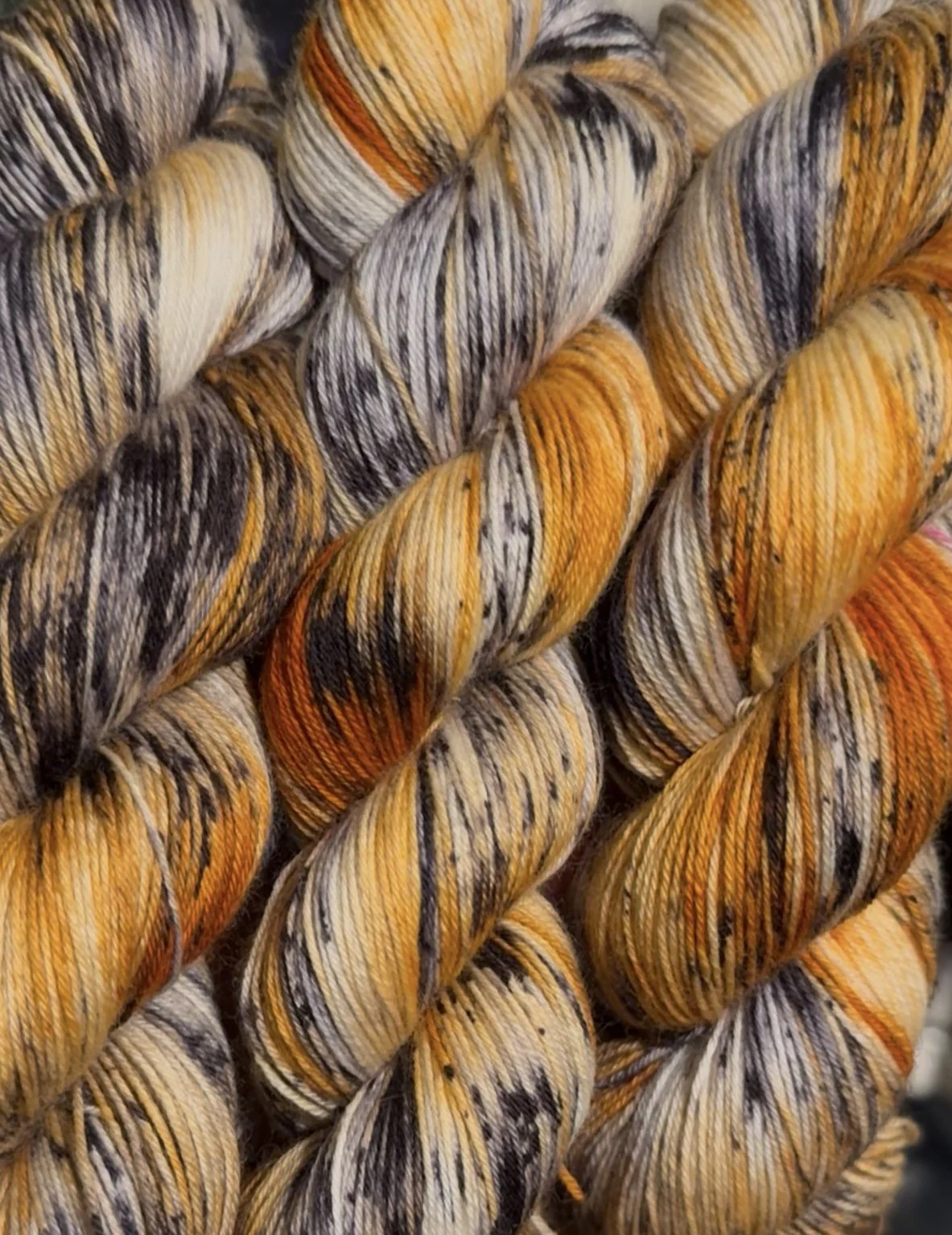 Close-up of multi-colored yarn skeins with orange, beige, black, and grey stripes.