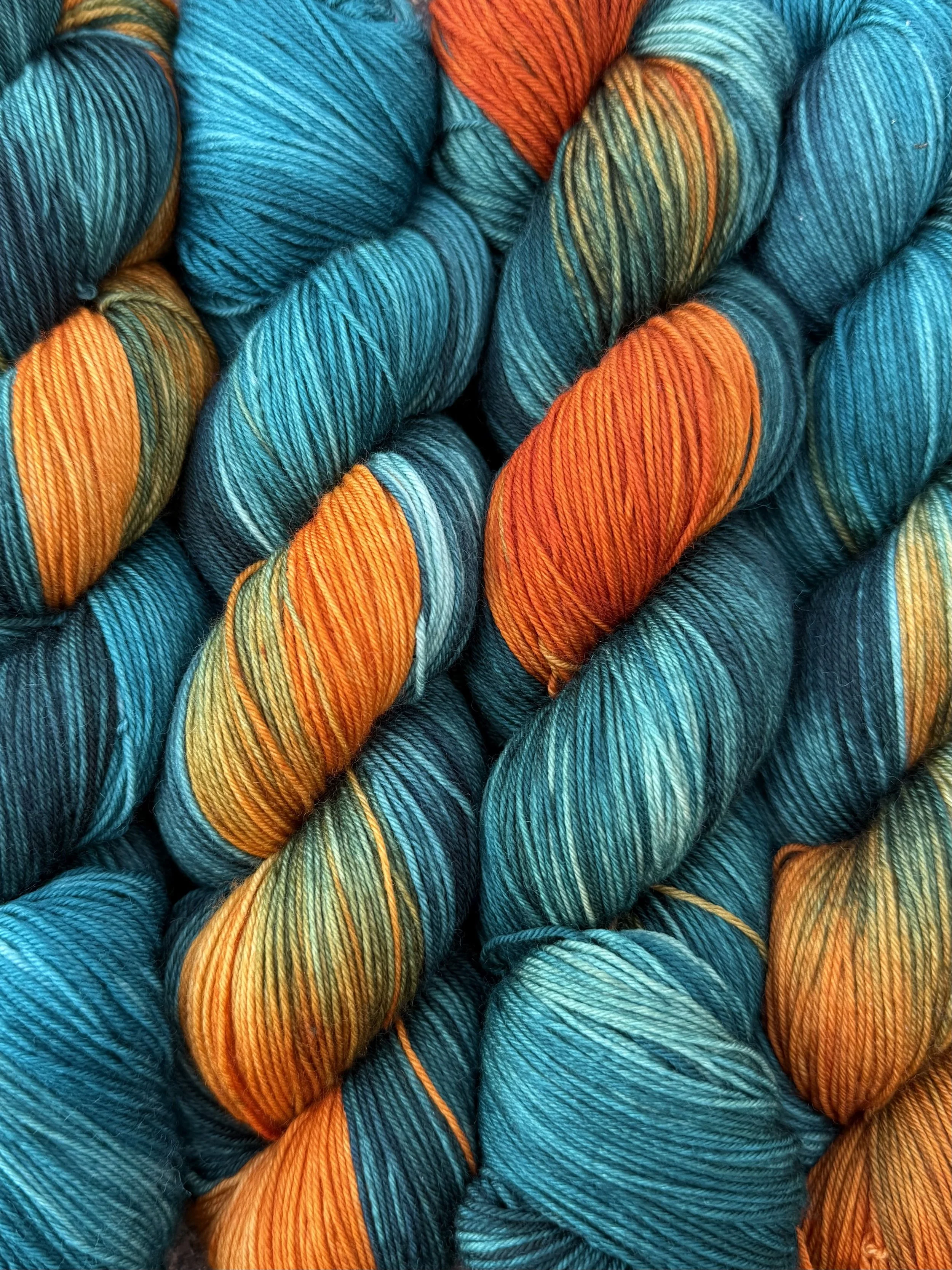 Multiple skeins of multicolored yarn in shades of teal, orange, green, and yellow, tightly wound and arranged in overlapping bundles.