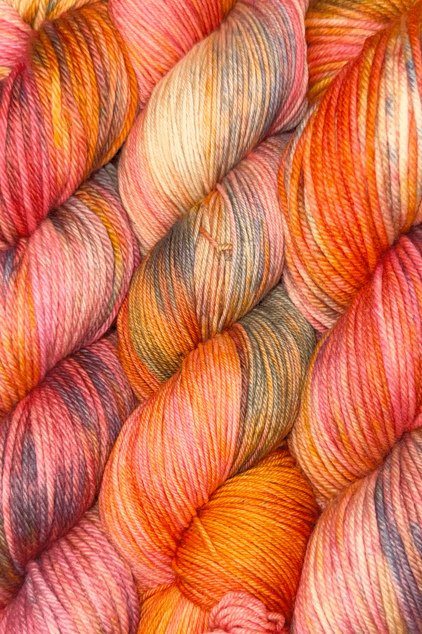 Close-up image of colorful yarn skeins in pink, orange, yellow, and purple shades, arranged in a coiled pattern.