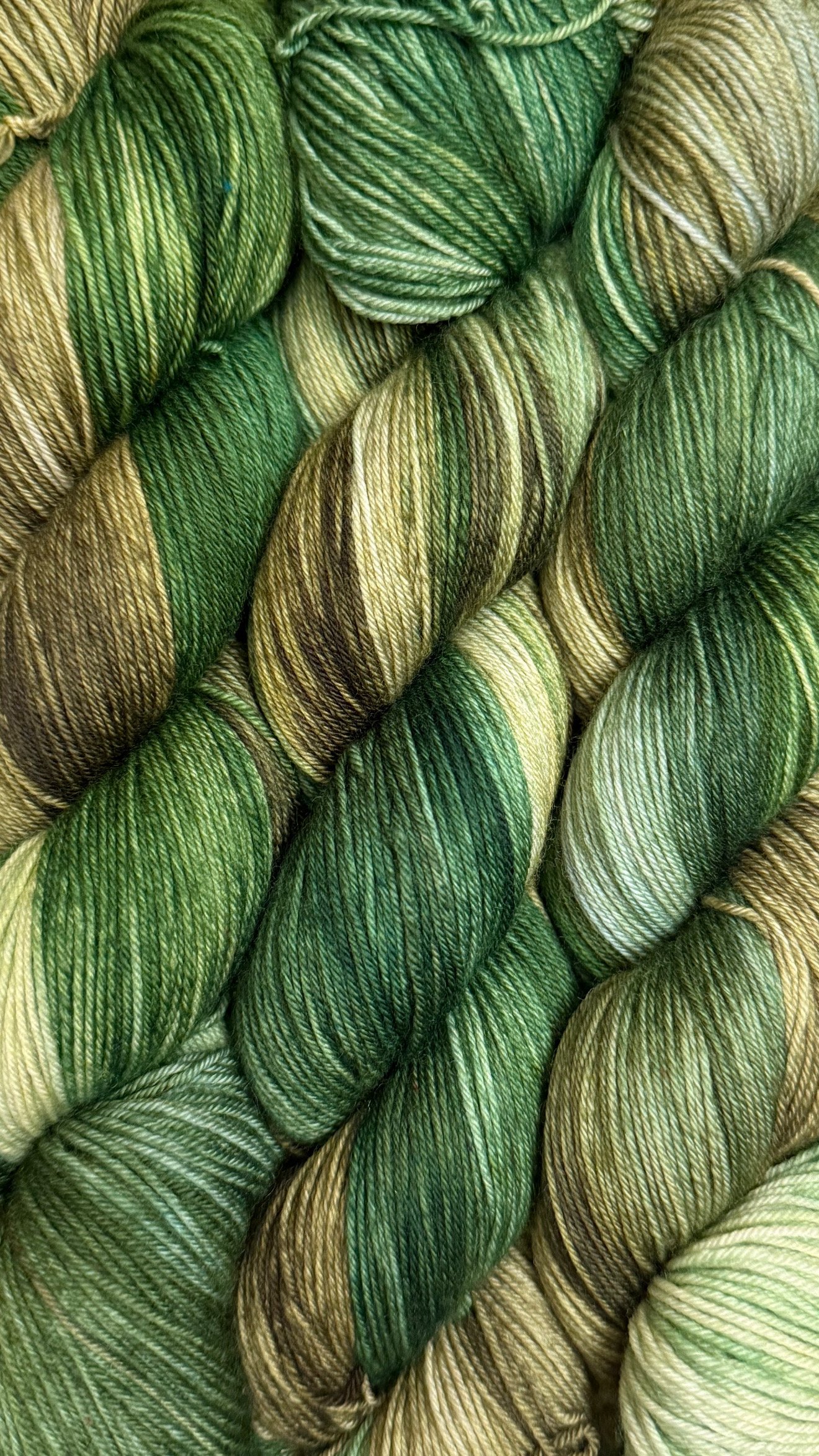 Close-up of multiple skeins of green and tan variegated yarn.