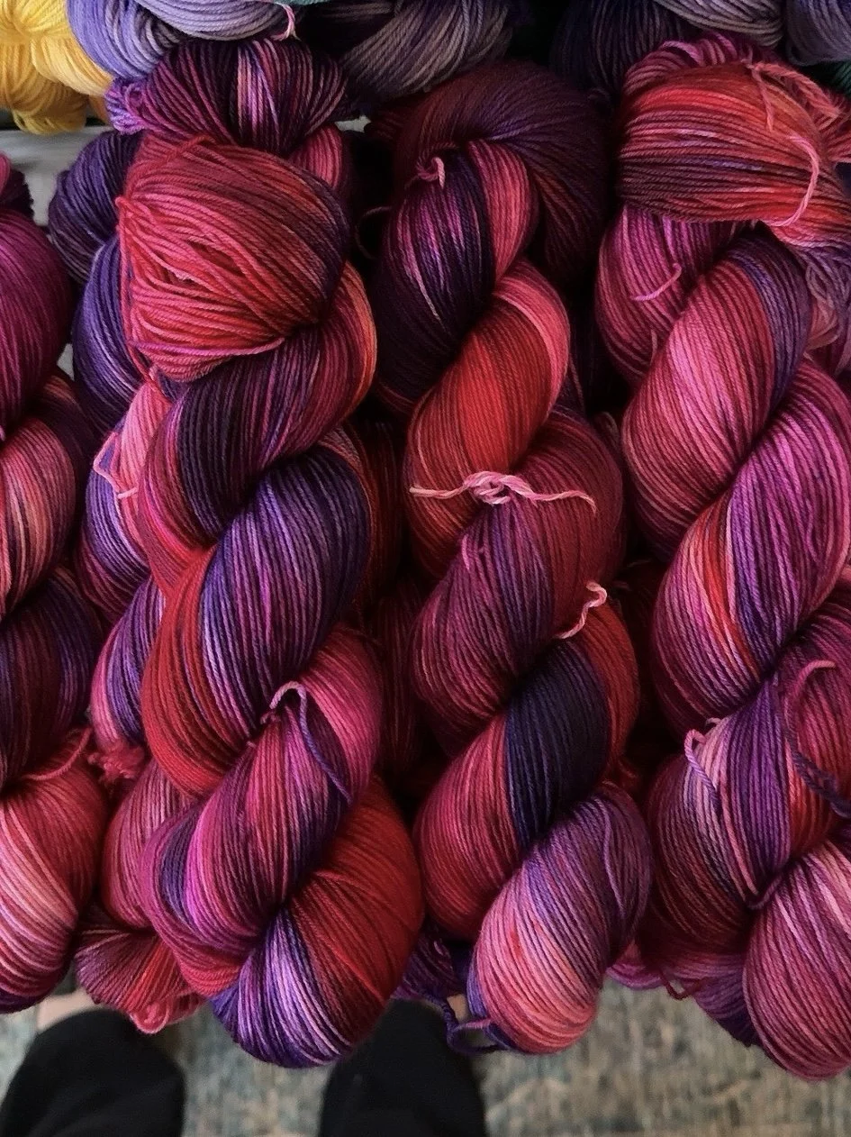 Multiple skeins of multicolored yarn in shades of pink, purple, red, and black, twisted into balls.