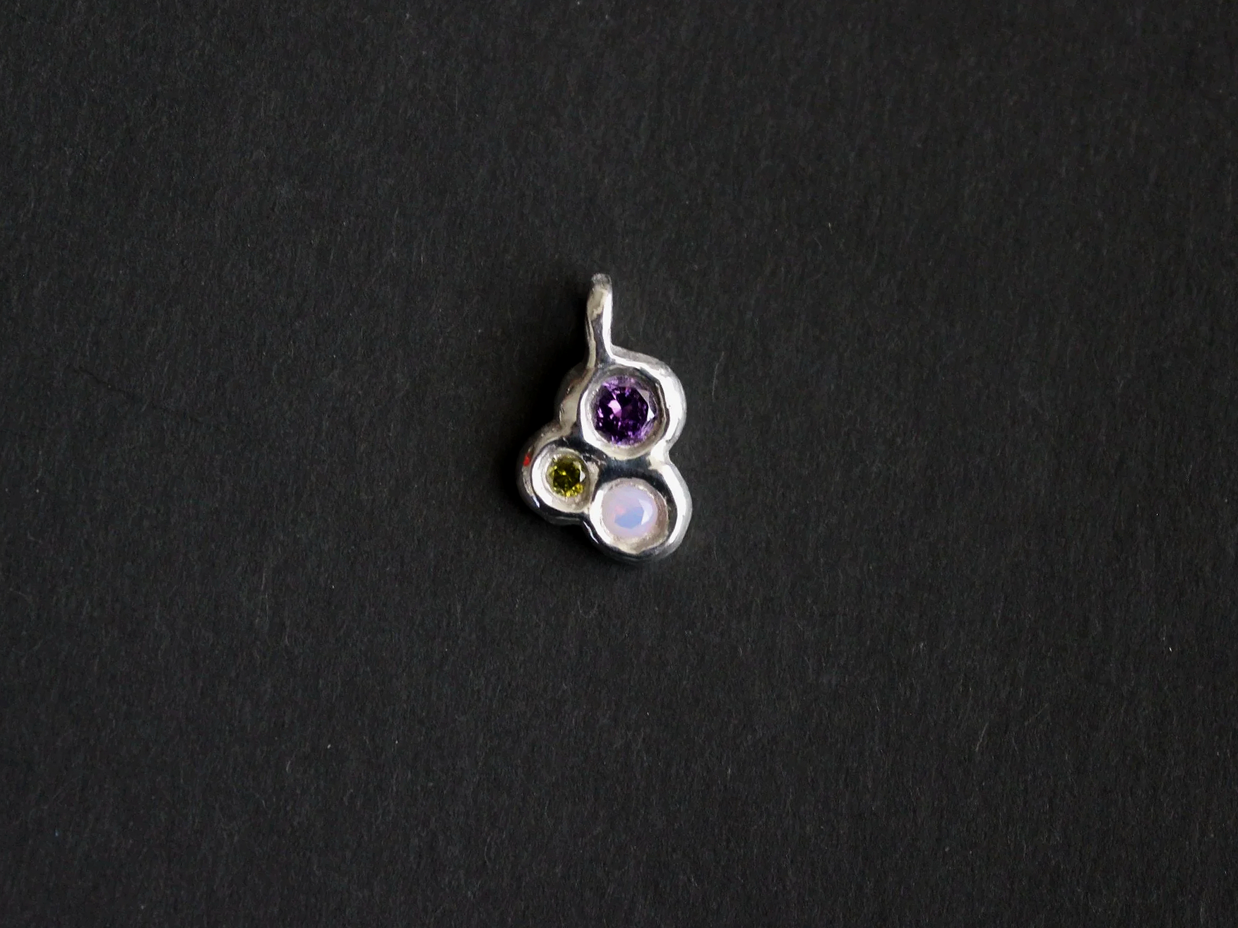 Silver pendant with purple, green, and light pink stones on a black background.