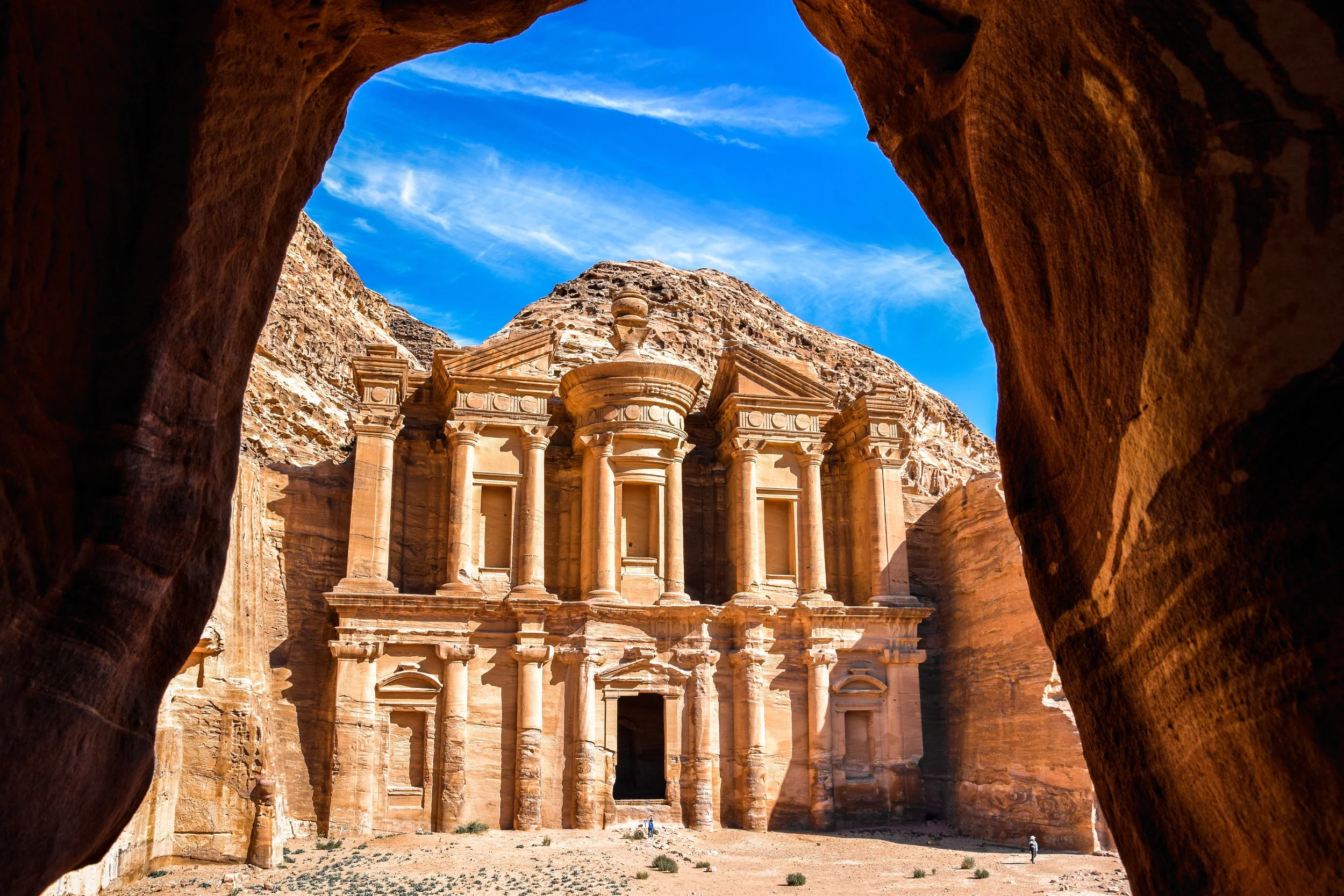 The ancient rock-cut city of Petra, Jordan, showcasing the iconic Al-Khazneh (The Treasury) carved into red sandstone cliffs with a bright blue sky overhead.