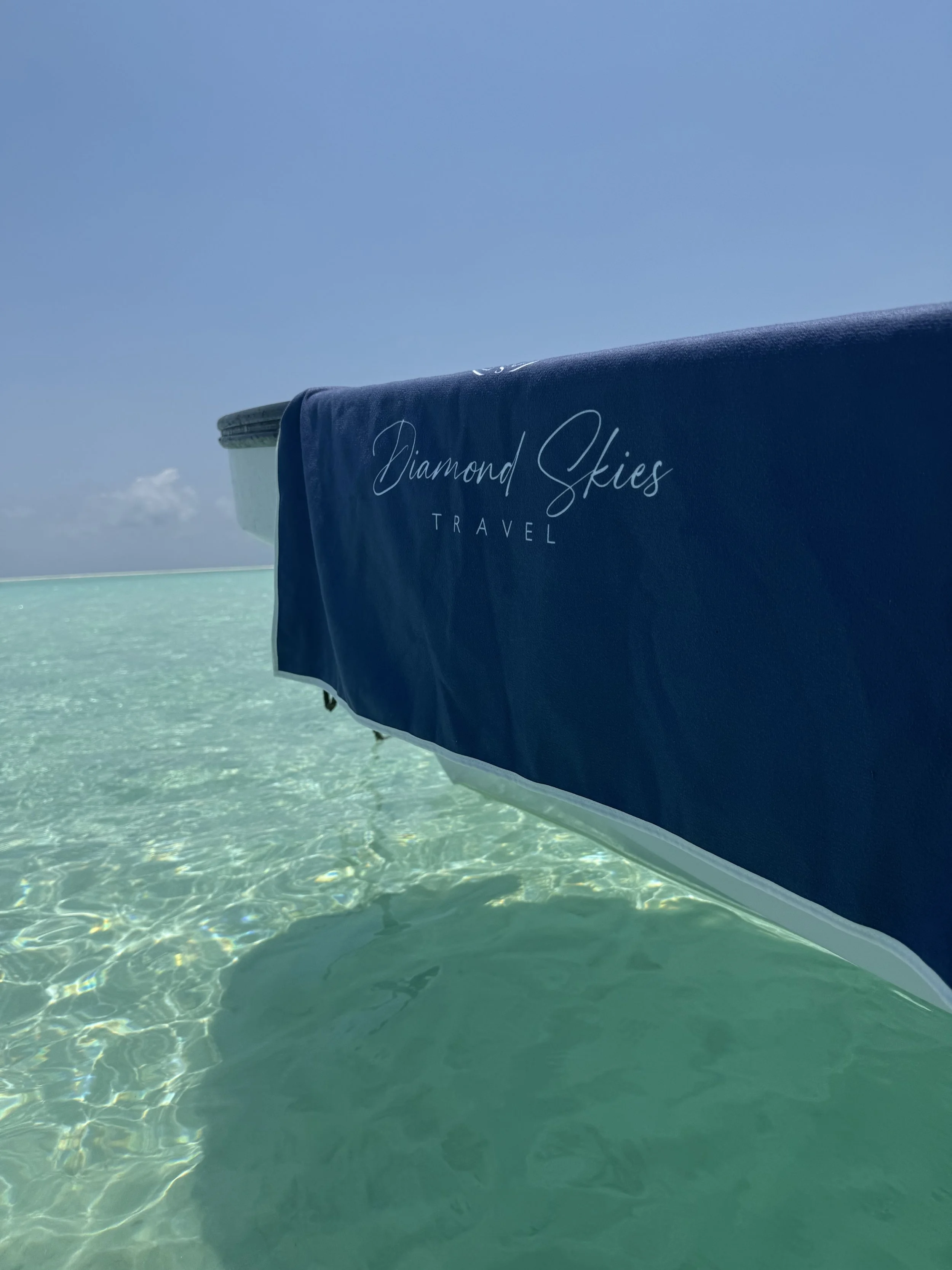 Close-up of a blue boat cover with the words 'Diamond Skies Travel' written on it, floating on clear turquoise water under a blue sky.