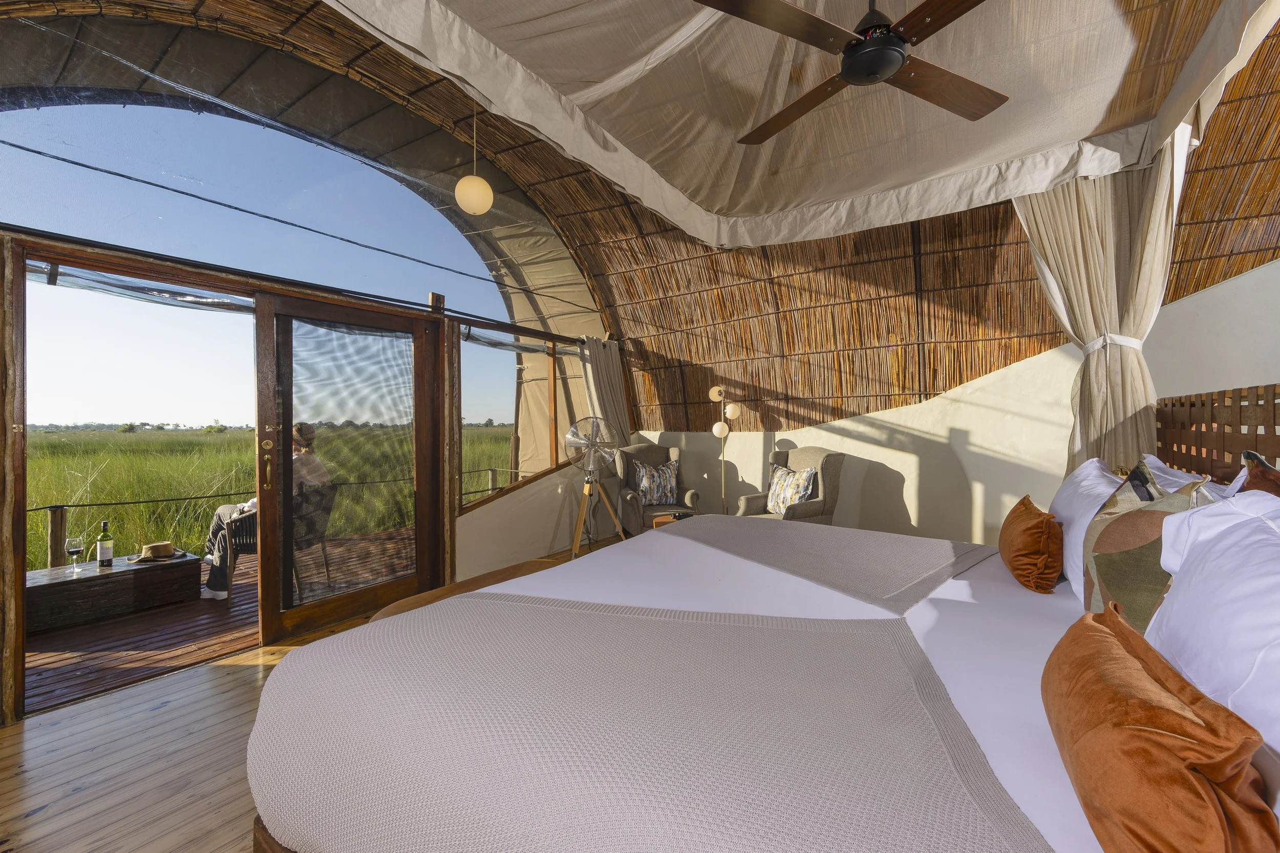 Elegant safari cabin interior with a woman sitting on the decking, viewing the African savanna