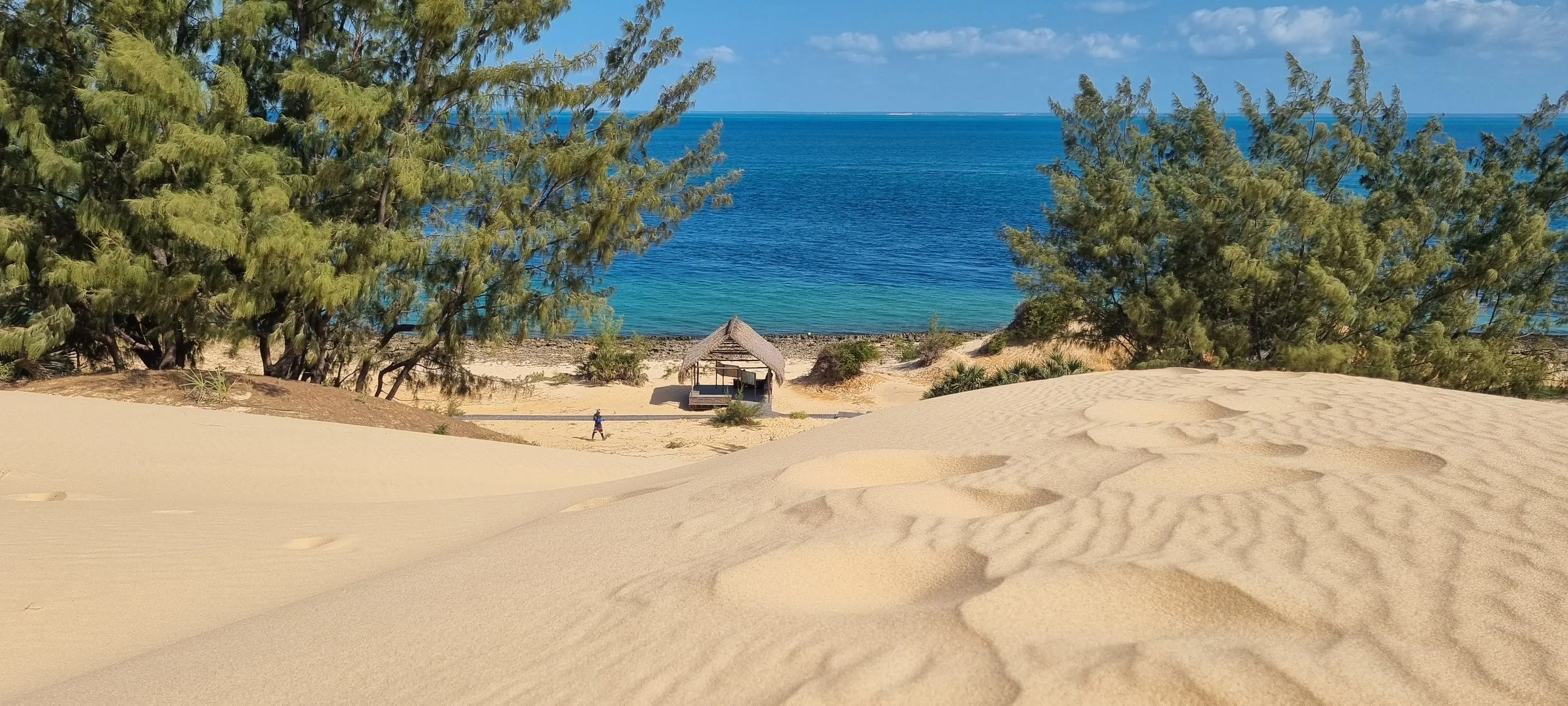 A thatched hut nestles between golden dunes and turquoise waves on Mozambique’s serene shoreline.
