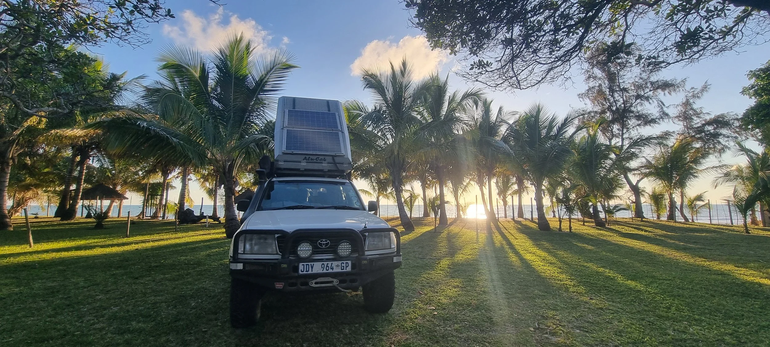 A white Land Cruiser with rooftop tent rests under golden light near Mozambique’s coast