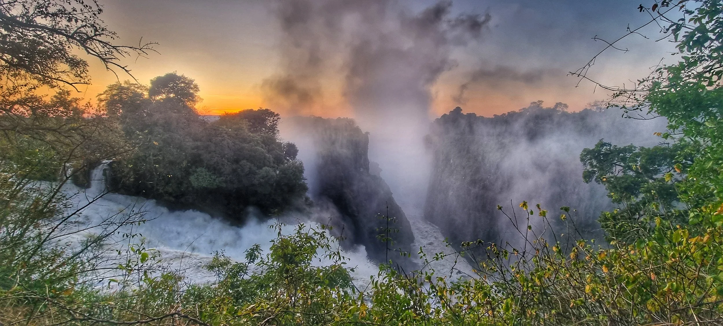 Sunrise over Victoria Falls in Zimbabwe, showcasing misty waterfalls and vibrant morning sky