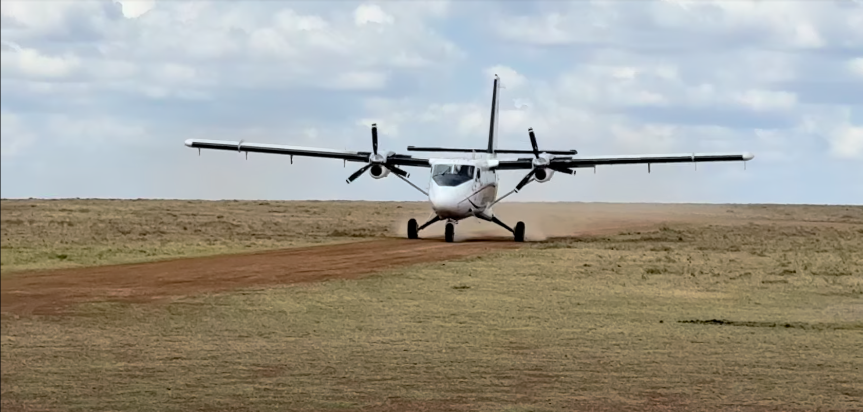 A twin-prop plane kicks up dust as it lands on a remote Kenyan airstrip