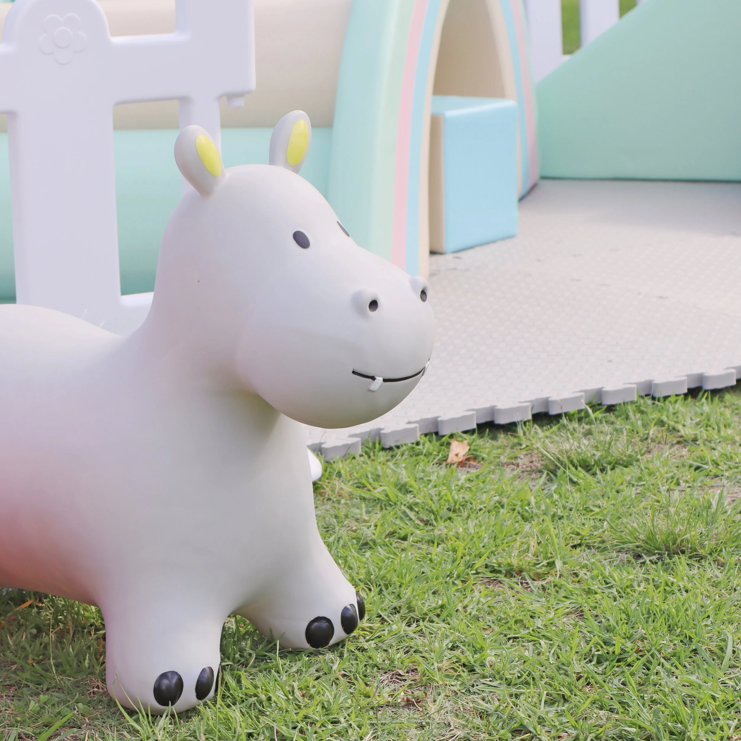 A white, cartoon-style animal figure resembling a hippo or similar creature, placed outdoors on grass near a colorful playground structure.