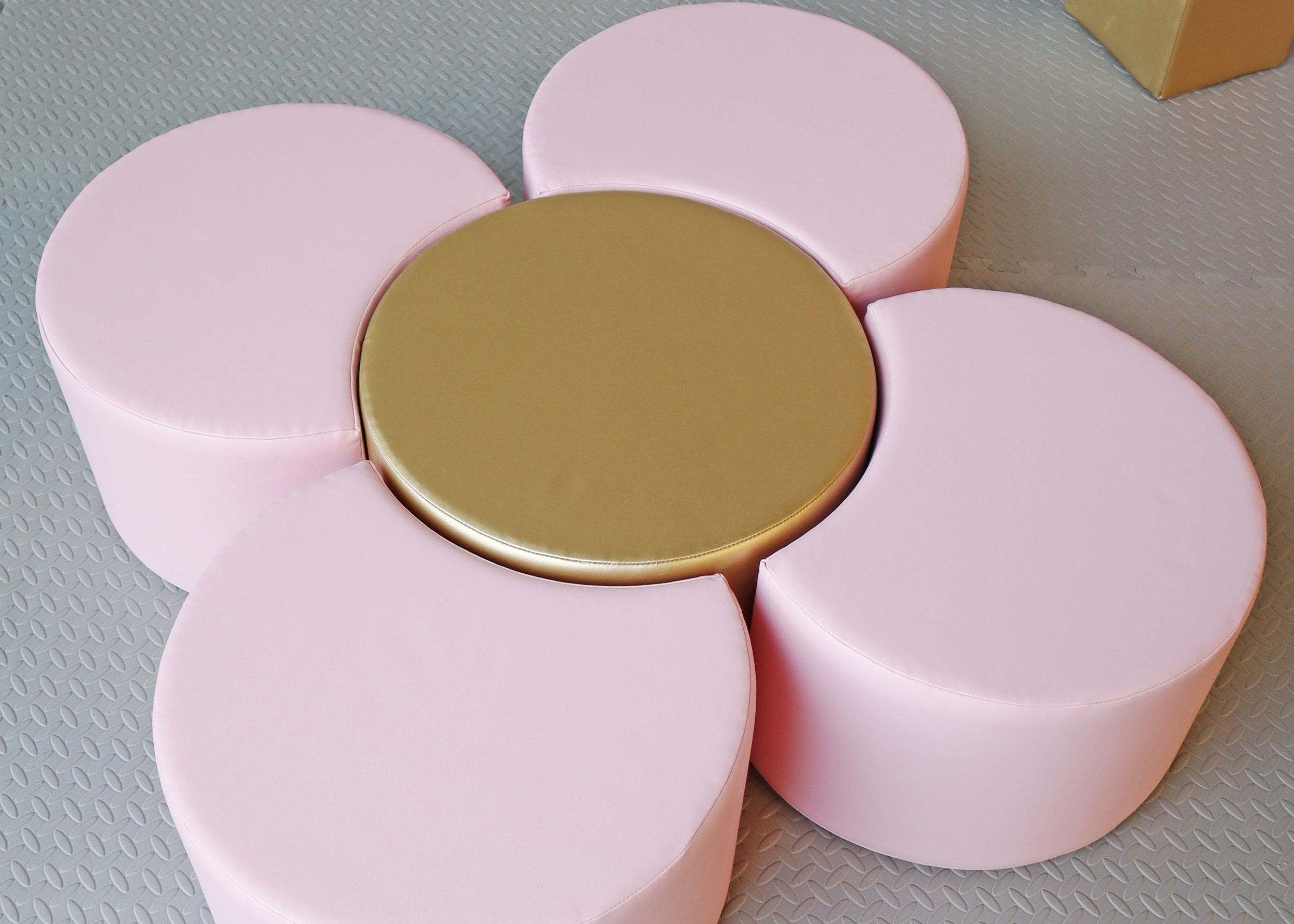 Pink and gold round stools arranged in a circular pattern on a textured gray floor.