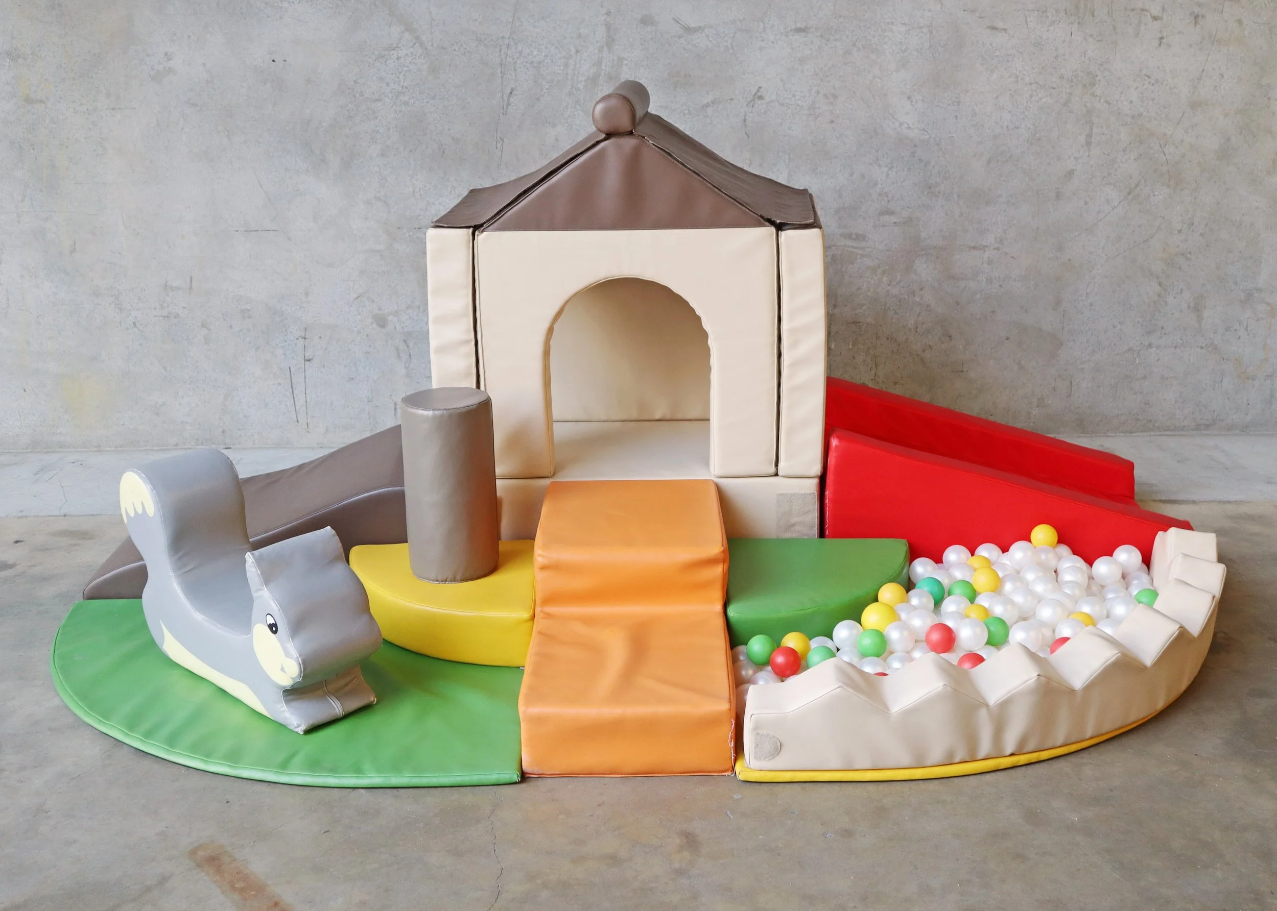 Colorful indoor children's soft play set with a ball pit, slide, and cushioned structures.