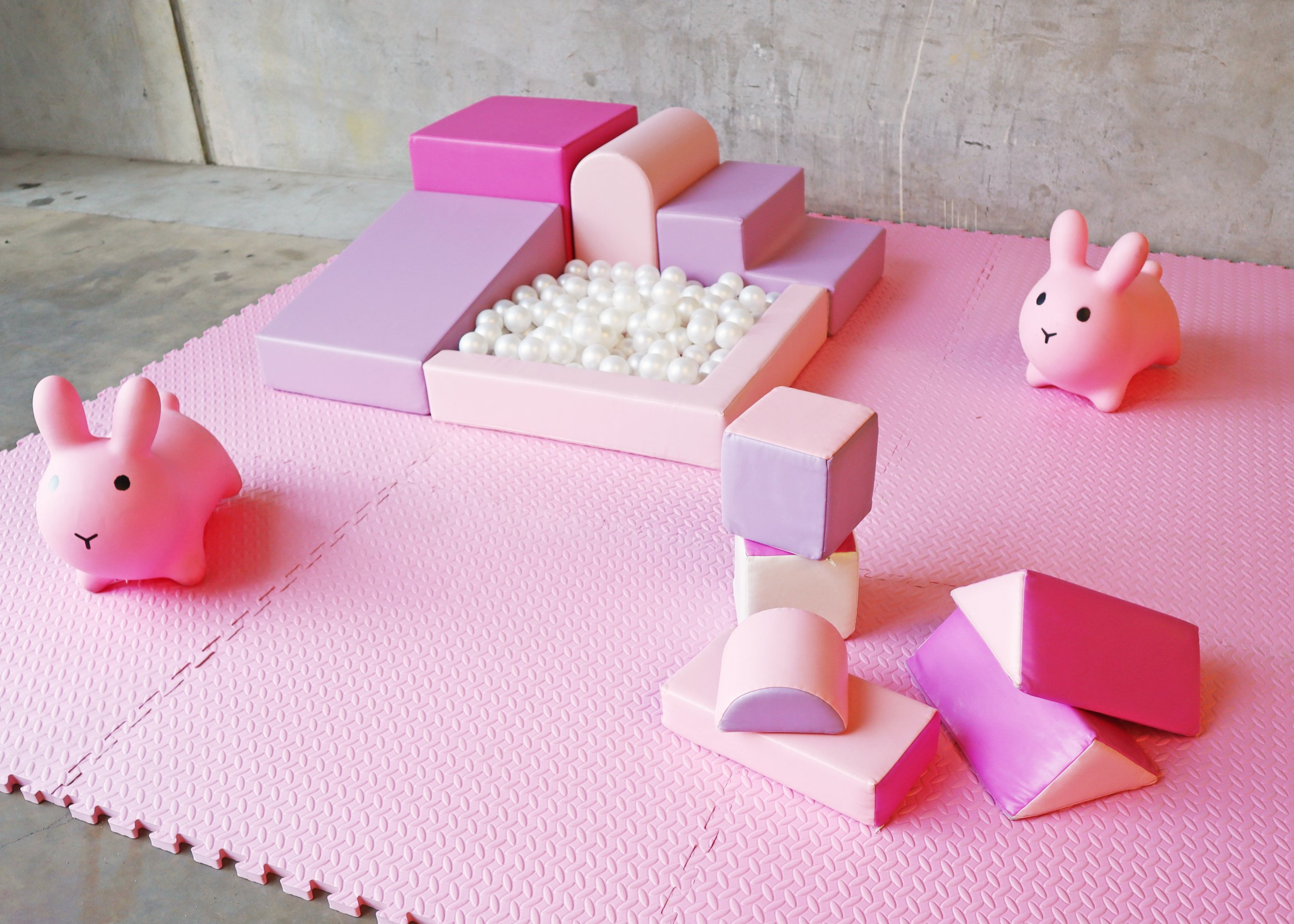 Pink and purple foam blocks and a ball pit with pearl-like balls on a pink foam mat, with two pink bunny-shaped toys nearby.