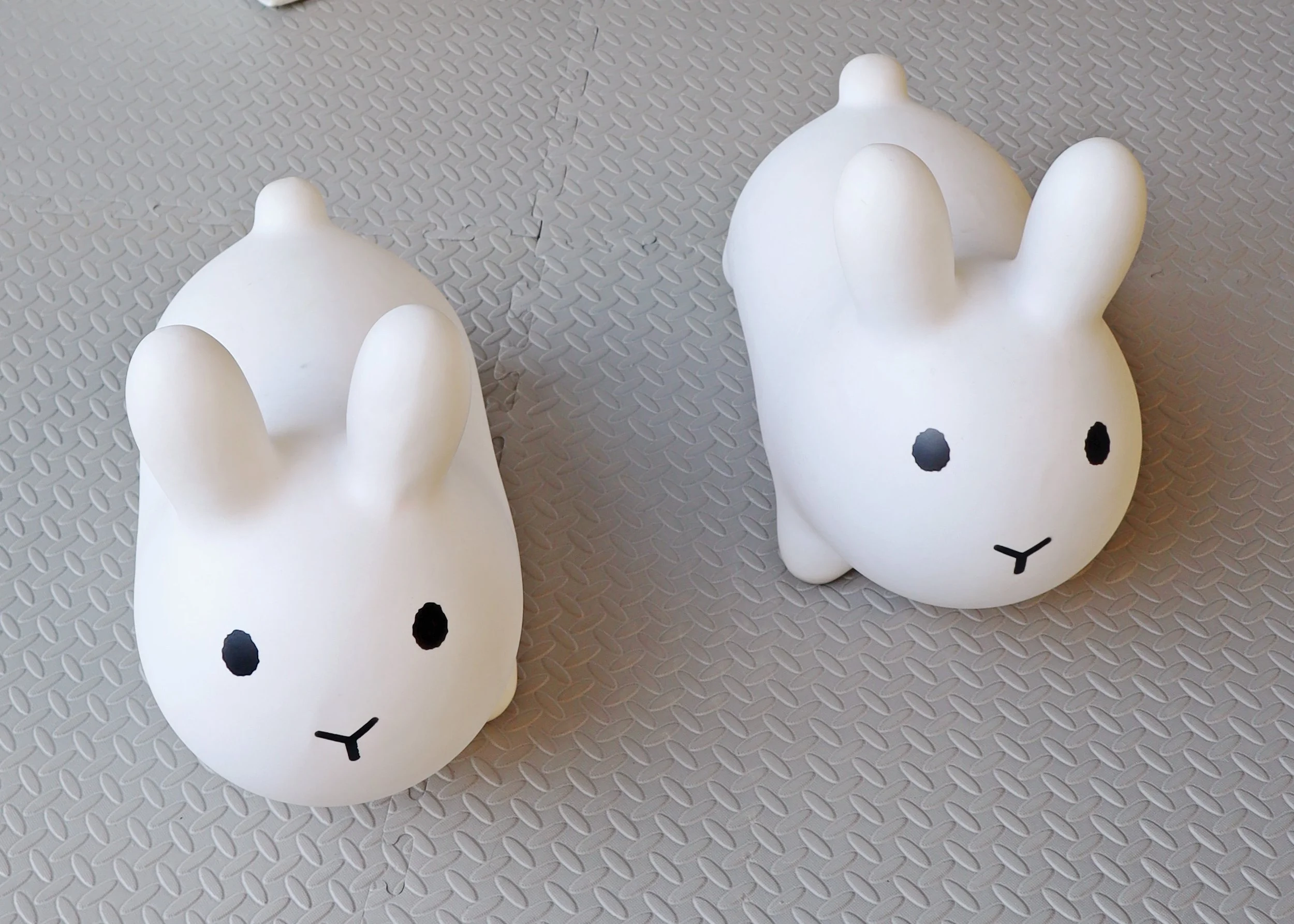 Two white bunny-shaped objects with black eyes and small mouths on textured gray surface.