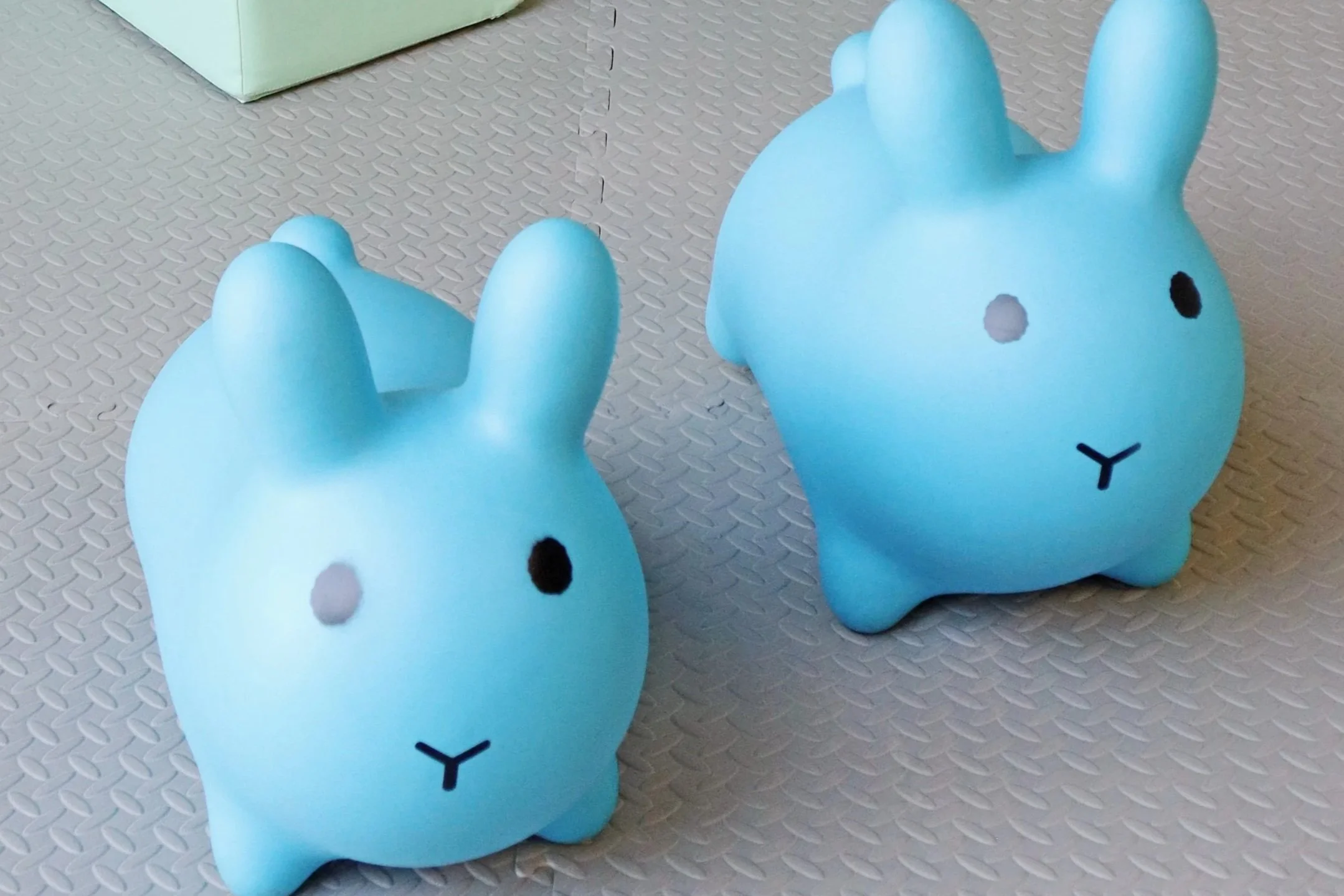 Two blue rabbit-shaped figurines with minimal facial features on a textured surface.