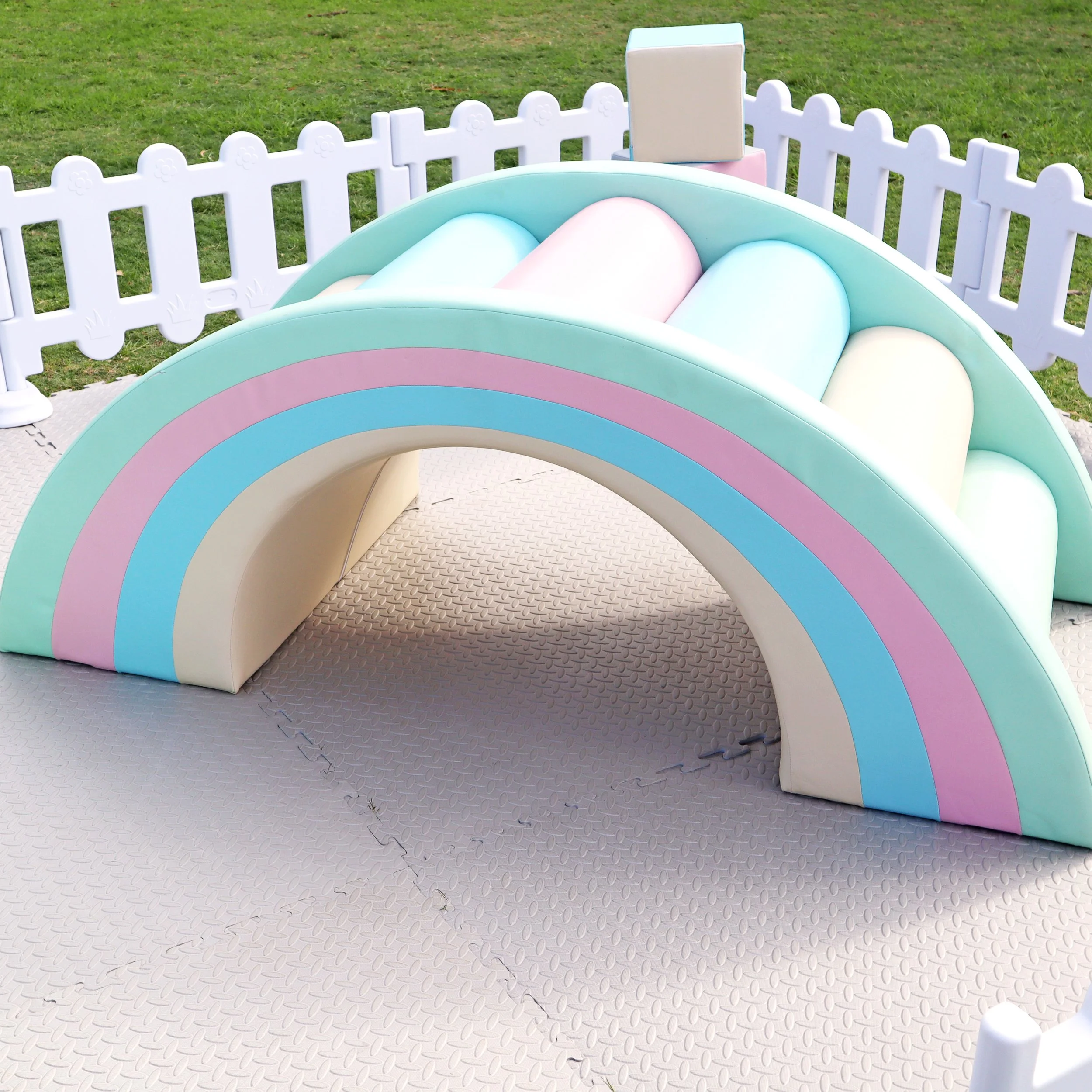 Colorful rainbow-shaped playground structure with a white picket fence background and grassy area.