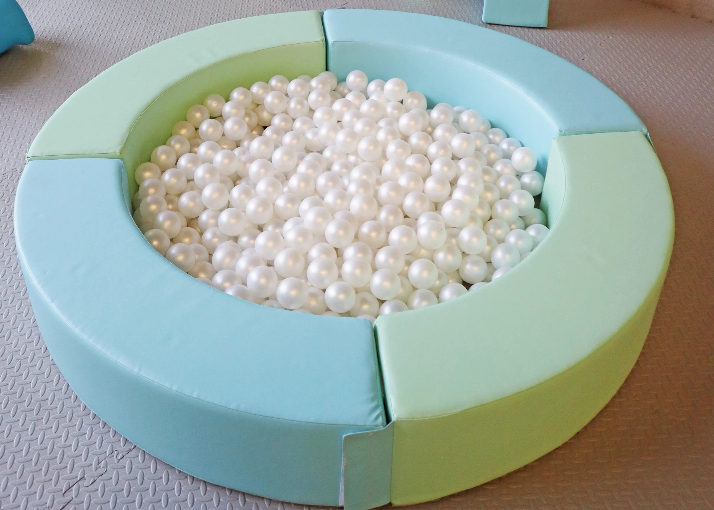 Colorful padded circular play area filled with white plastic balls.