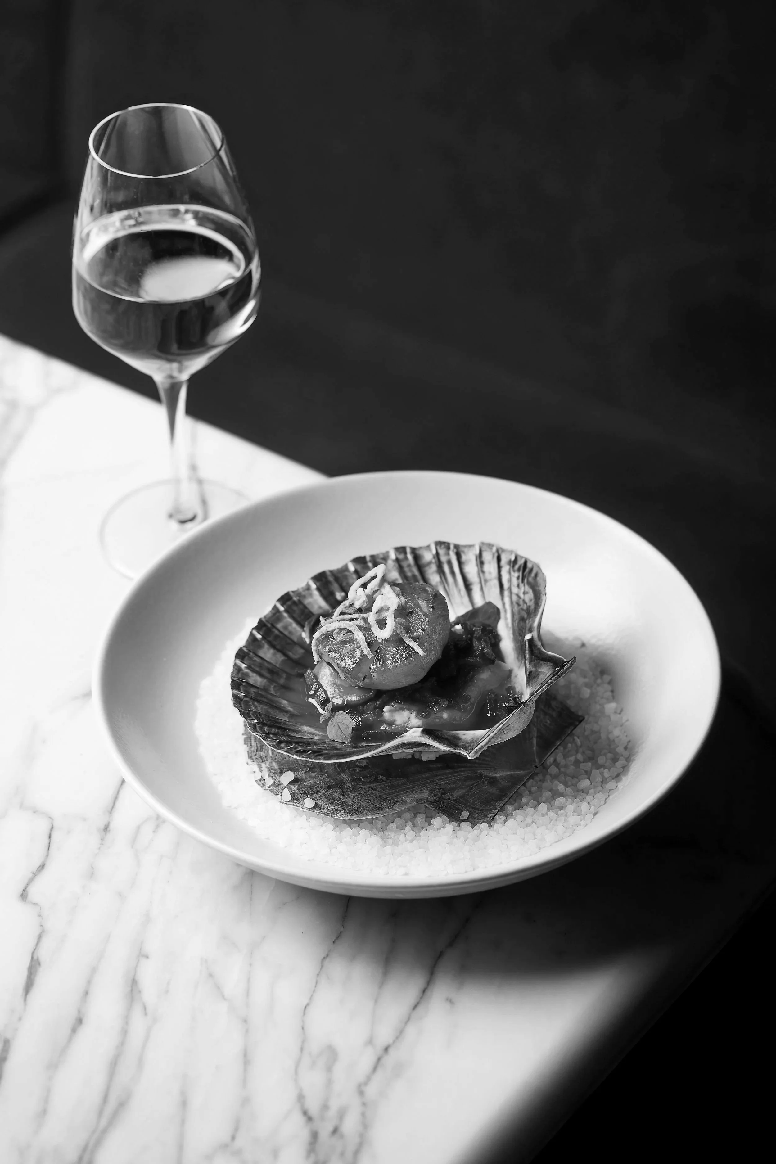 A glass of white wine and a plate with a seafood dish on a marble table.