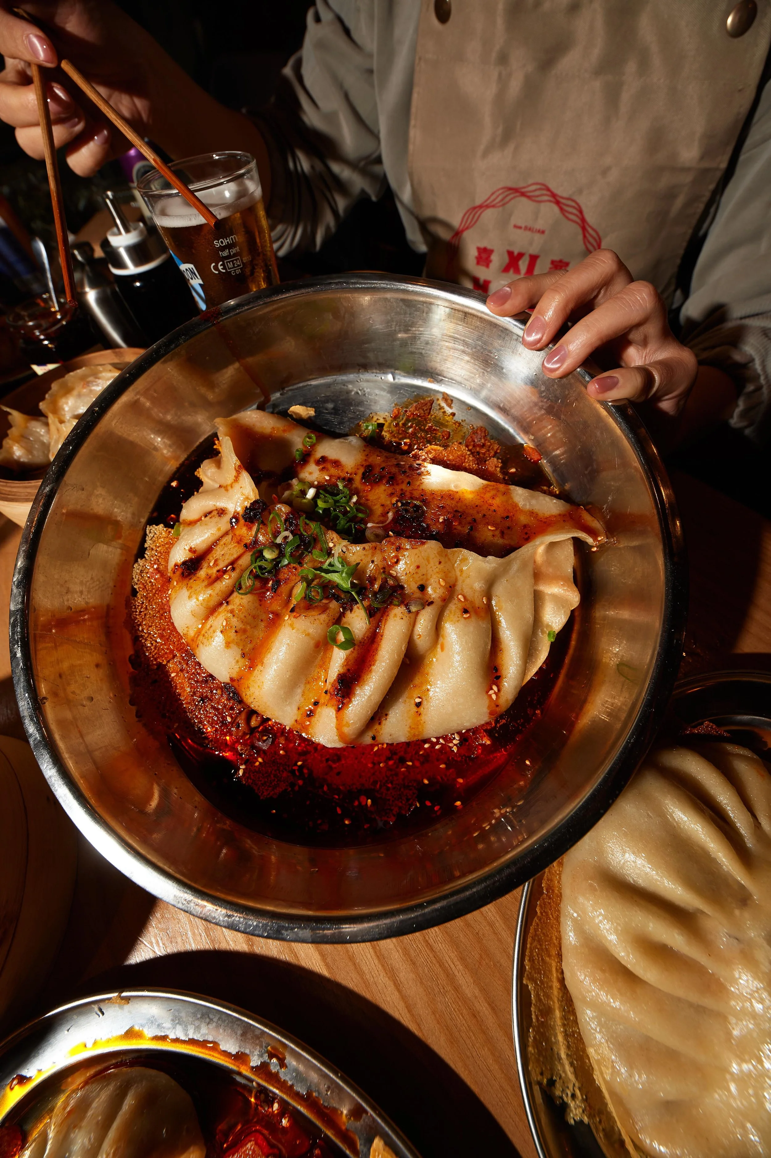 Close-up of a bowl of Chinese dumplings with chili oil and green onions, with chopsticks. One of our client success stories at Amy Williams Consultancy is Noodle and Beer Restaurants in Chinatown and Spitalfields. Lots of PR Brand Coverage achieved