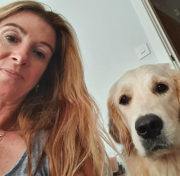 A woman with long hair taking a selfie with a golden retriever dog inside a home.