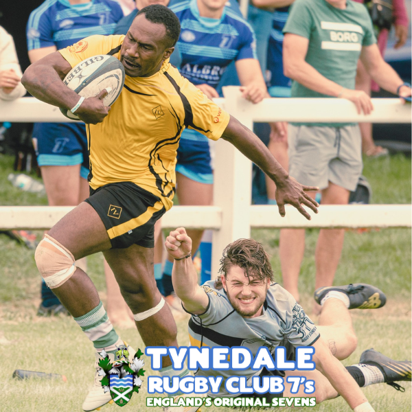 A rugby player in a yellow jersey runs with the ball while an opponent in a gray jersey tries to tackle him on the ground, during a match at Tynedale Rugby Club.
