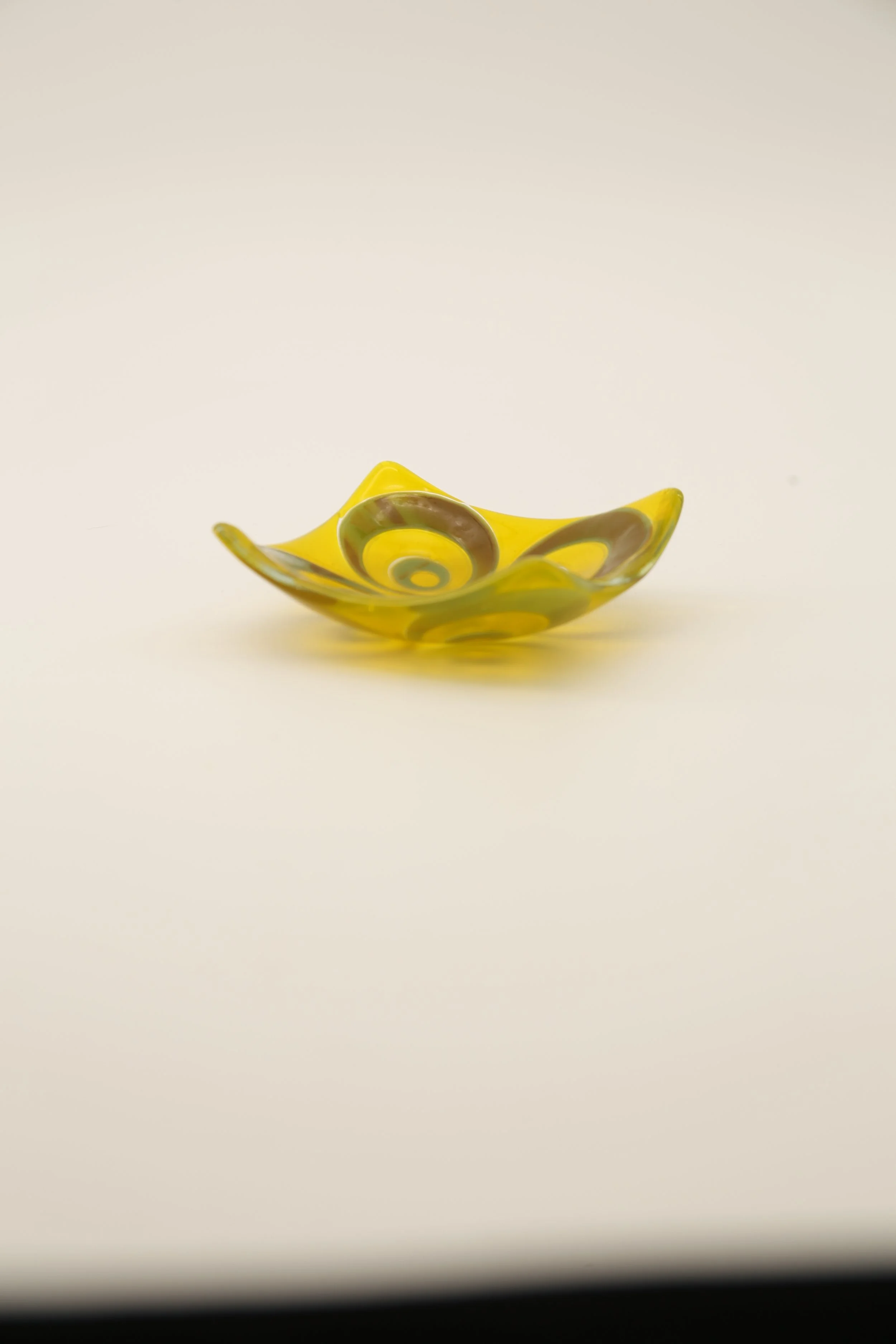 A small, yellow glass bowl with 60s/70s decade abstract swirl patterns in green and brown, placed on a white background.