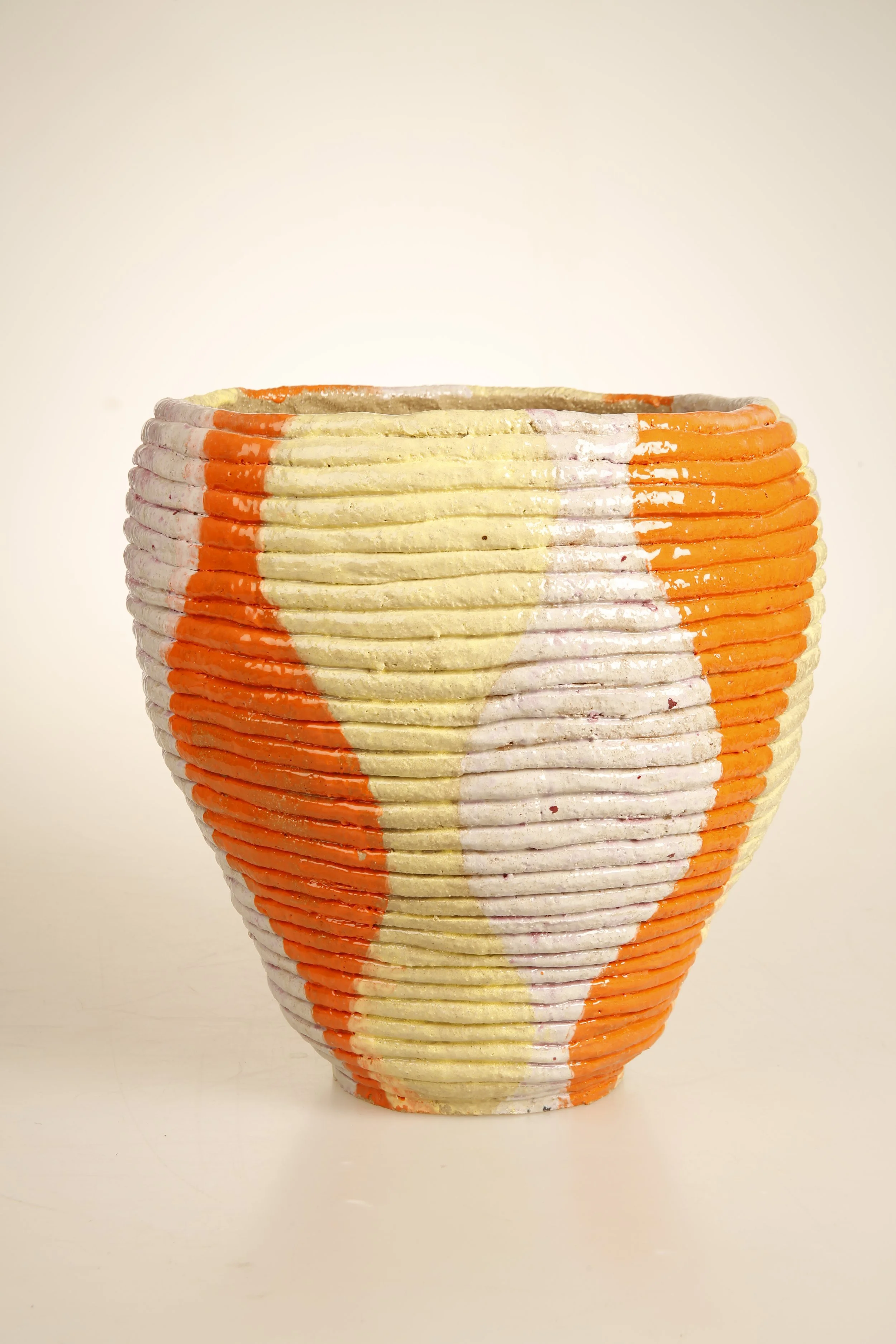 Colorful ceramic vase with 60s/70s decade horizontal ridges and painted in orange, yellow, white, and purple abstract patterns.