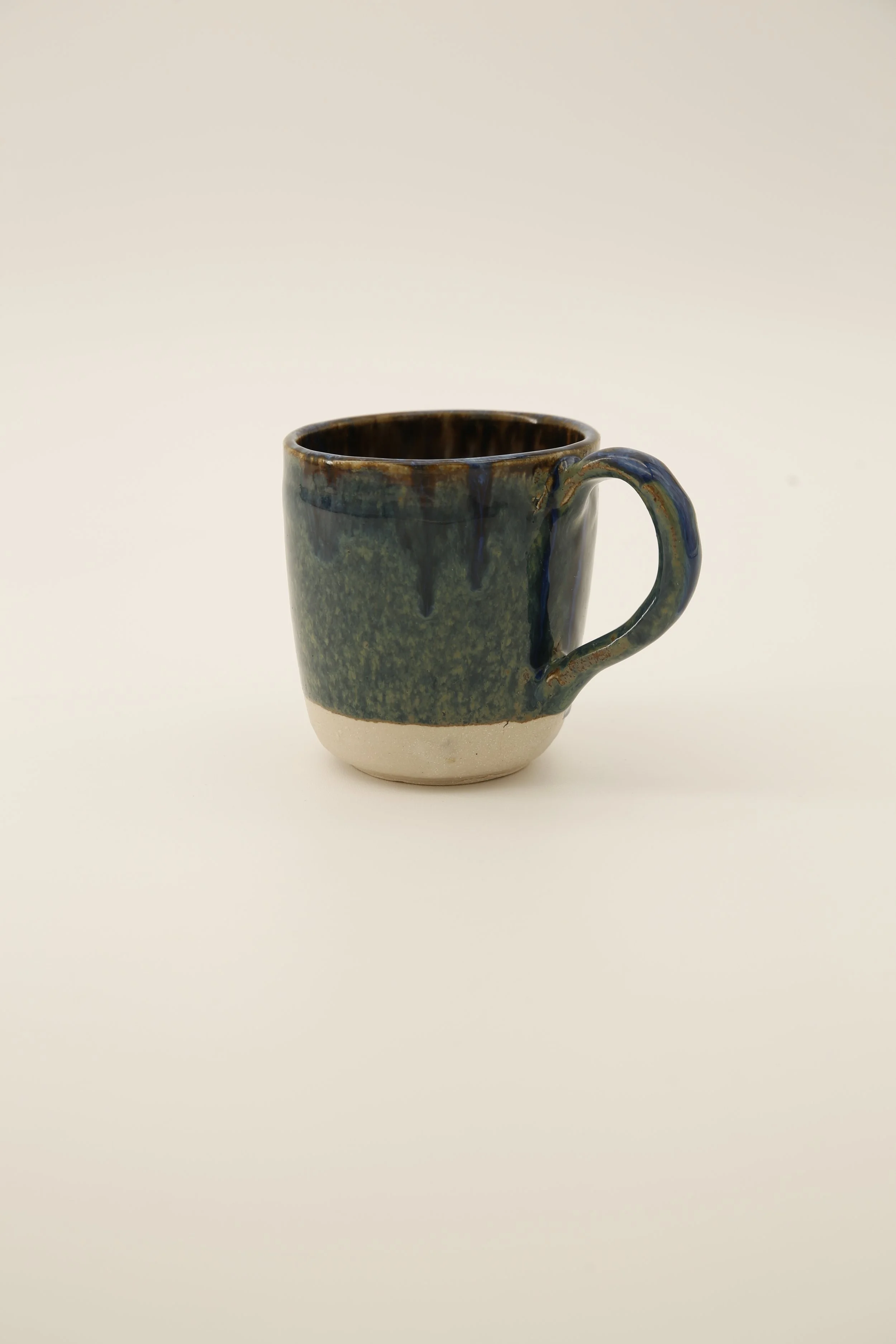 A ceramic mug with a green and blue glaze and a white base on a plain white background.