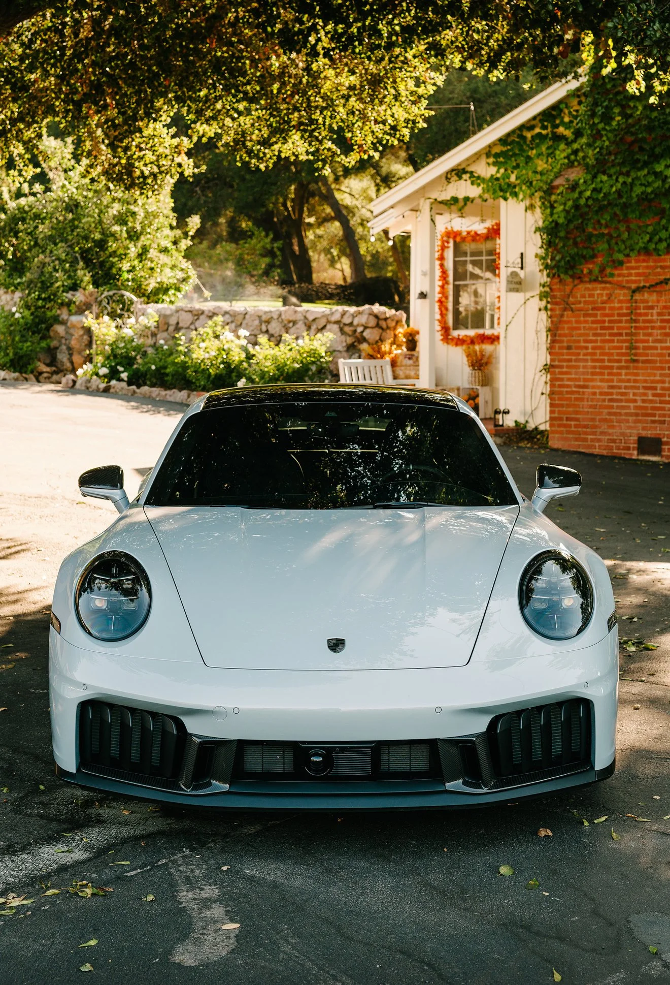 Front view of a white sports car parked outdoors near a house with autumn decorations and greenery.