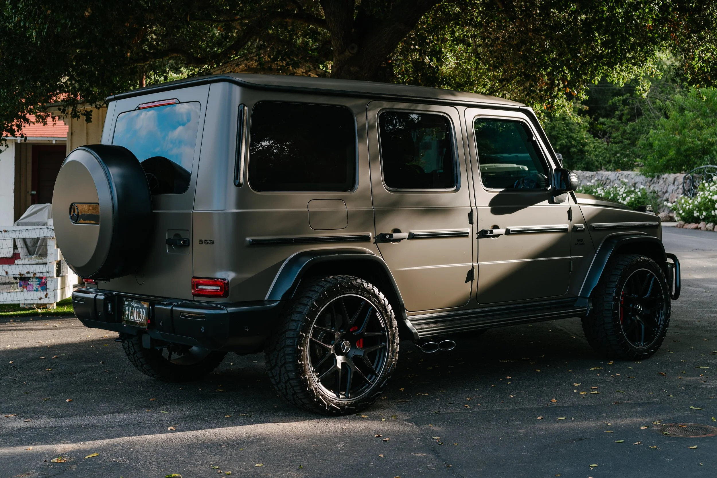 A matte gray Mercedes-Benz G-Class SUV parked on a driveway under a tree.
