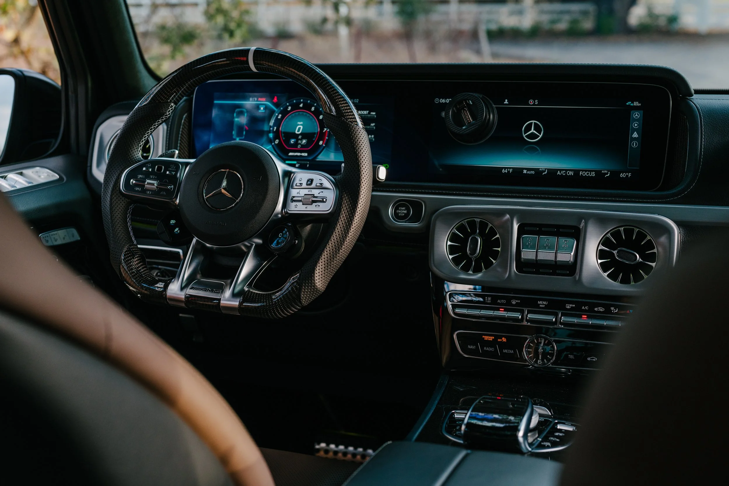 Interior of a luxury Mercedes-Benz vehicle showing a steering wheel, digital dashboard, and center console with controls and displays.
