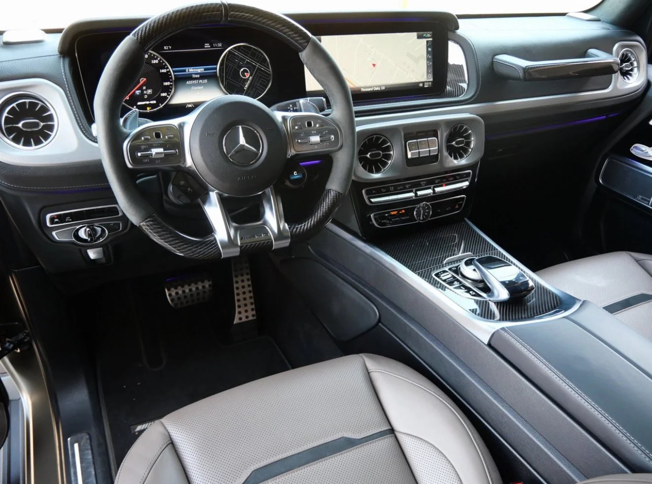 Interior of a modern Mercedes-Benz car showing the steering wheel, dashboard, infotainment screen, and center console with controls.