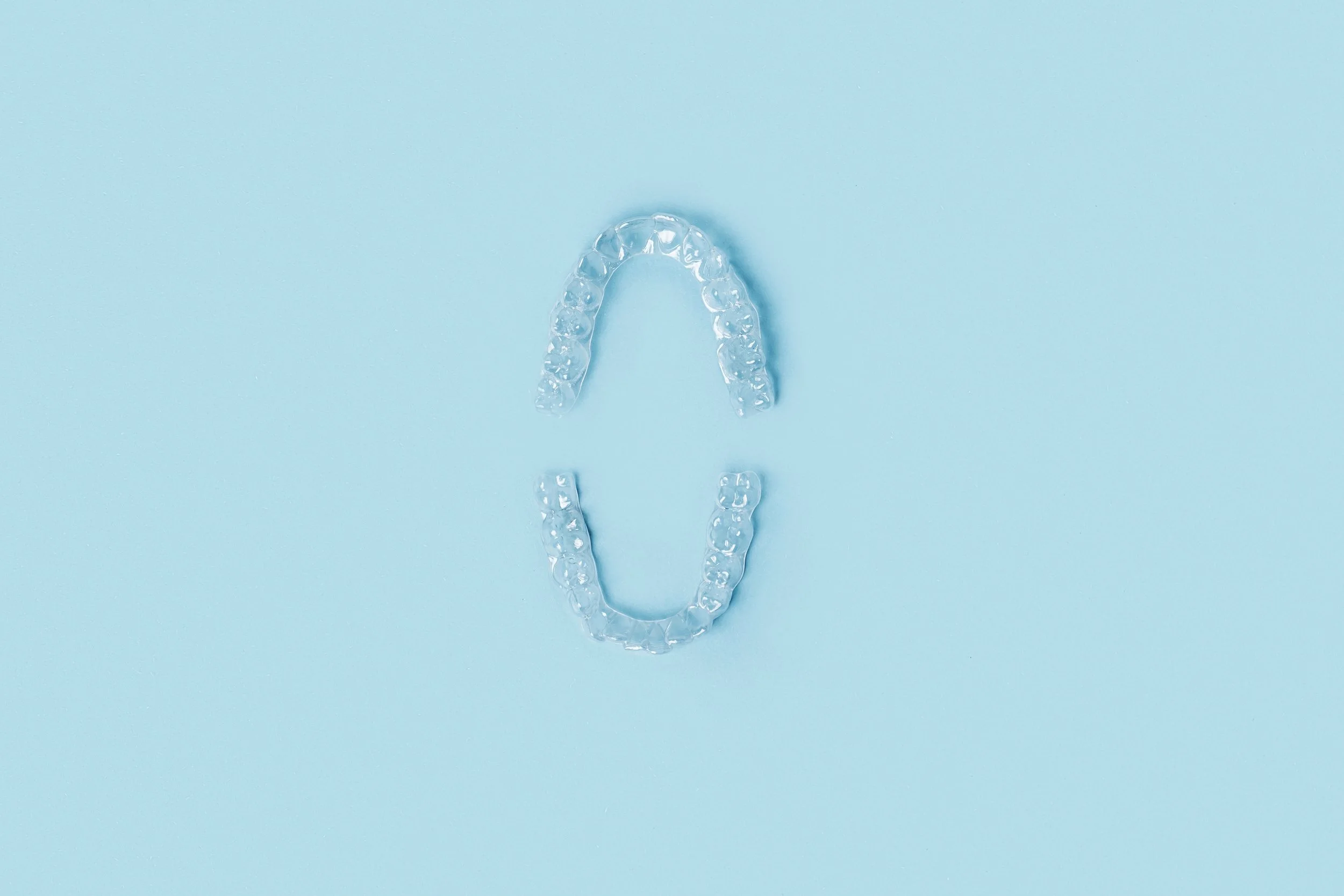 Clear dental aligners arranged in an oval shape on a light blue background.