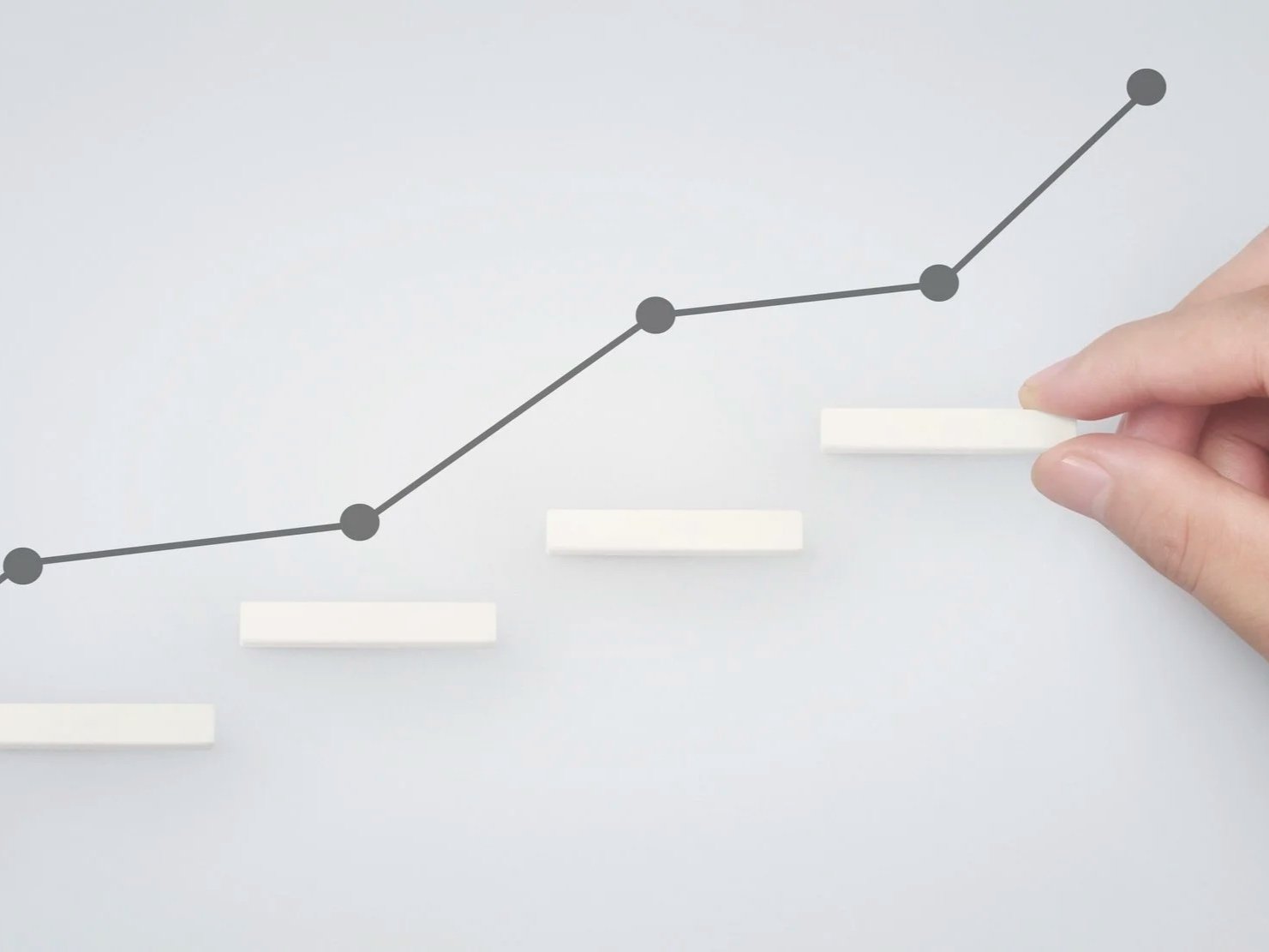 A hand moves a white marker in front of a gray line graph with black dots on a light gray background.